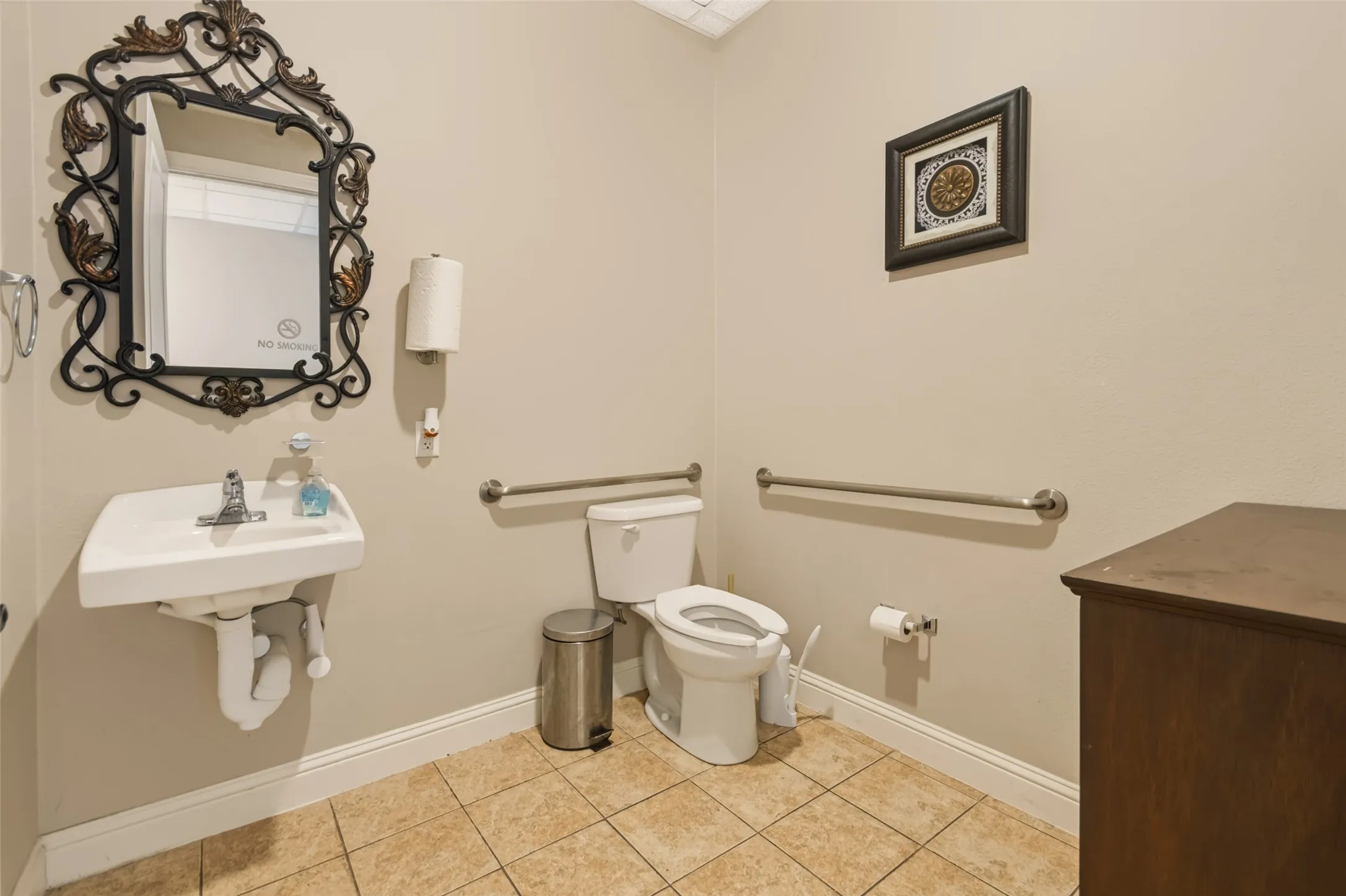 Wall-mounted sink with chrome faucet, ceramic tile flooring, and two stainless steel grab bars