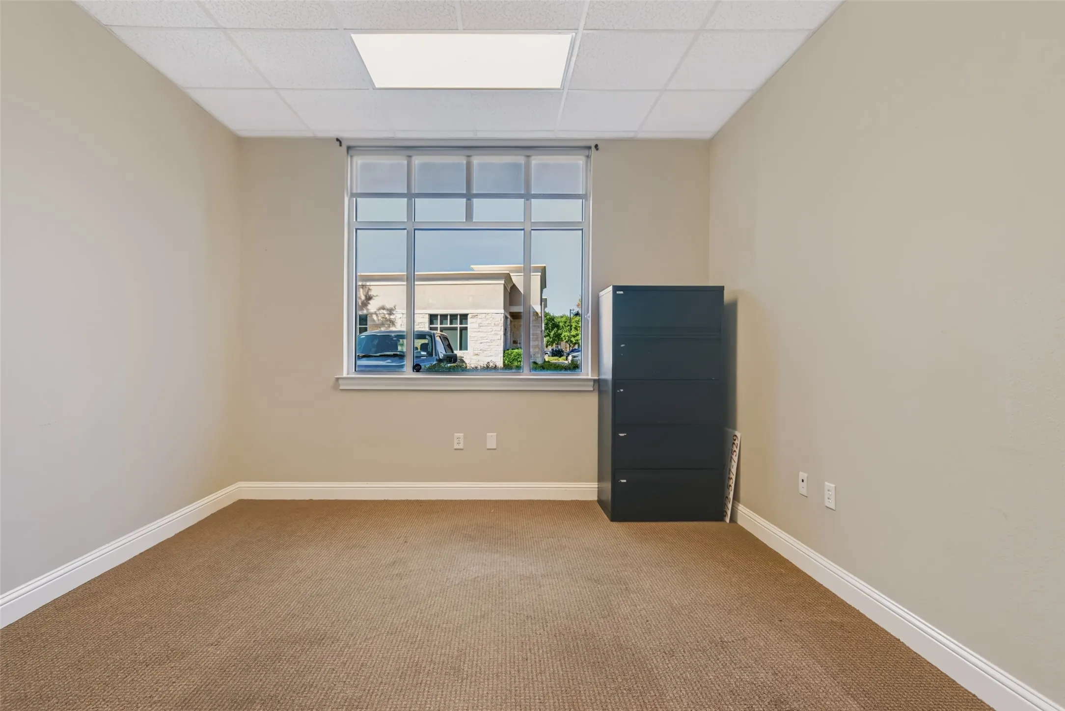 Wall-to-wall carpeting, neutral wall finishes, drop ceiling, and a large multi-pane window
