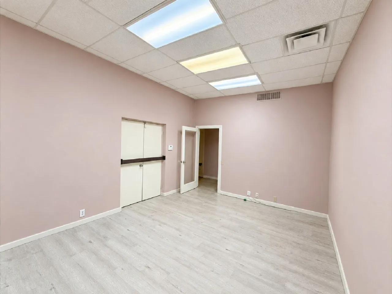 Light-toned wood-finish flooring, drop ceiling with integrated lighting, dual fire-rated doors, and a glass-paneled interior door