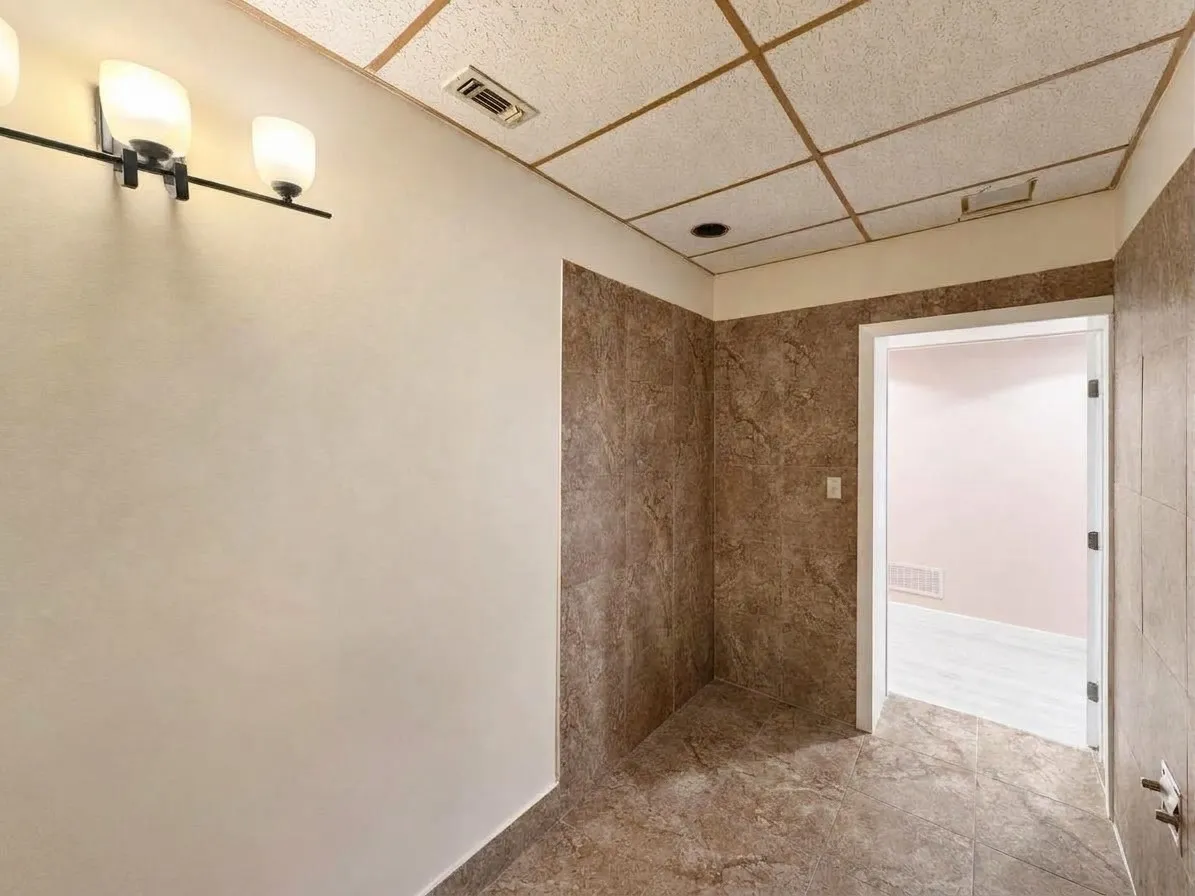 Recessed ceiling lighting, flush-mounted light fixture, full tile flooring, partial wall tiling, and a drop ceiling