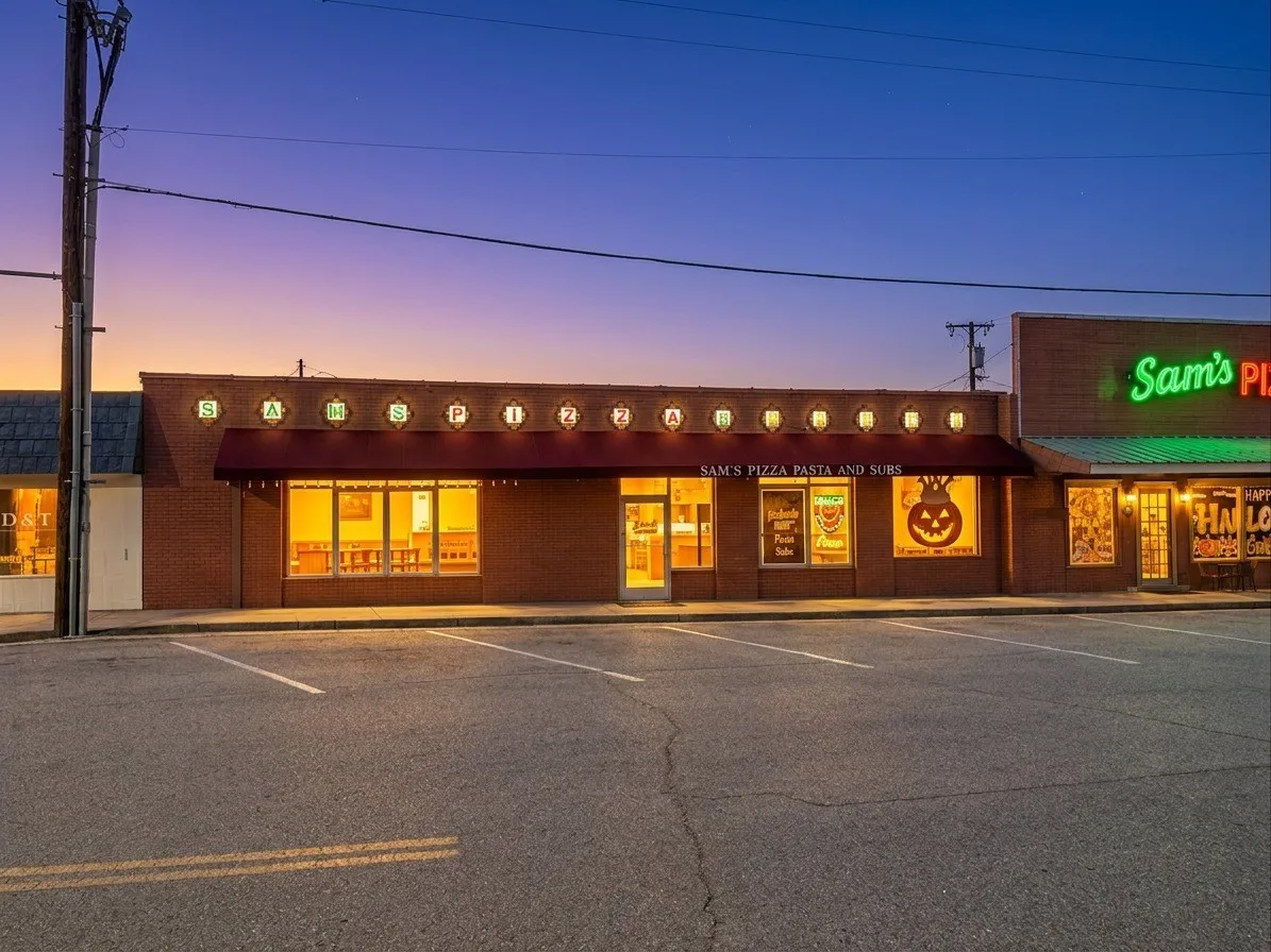 Brick storefront with multiple large display windows, a retractable awning, and exterior lighting