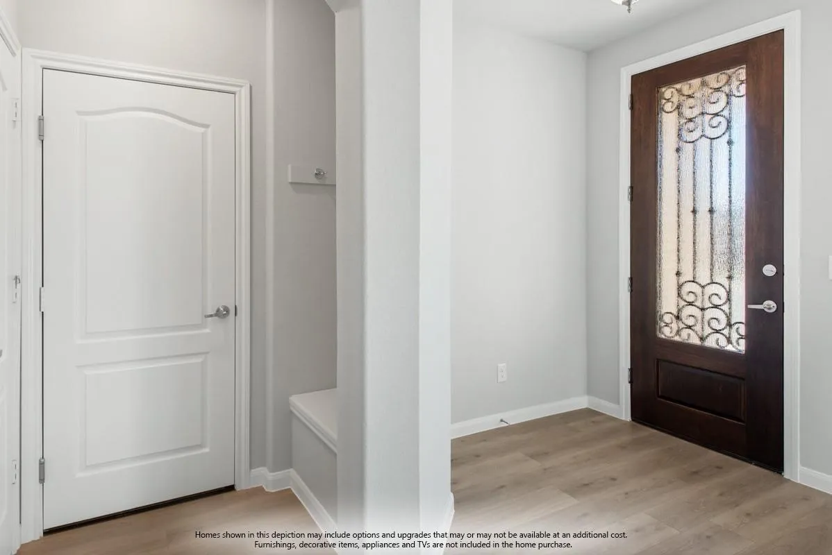 Wood-finish flooring, dark wood entry door with ornate wrought iron and frosted glass, white paneled interior door, and built-in bench