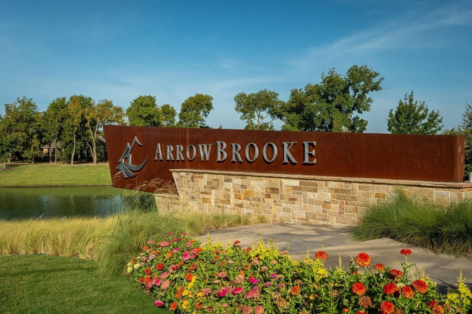 Stone-clad monument sign with metal lettering, bordered by manicured landscaping and a reflective pond