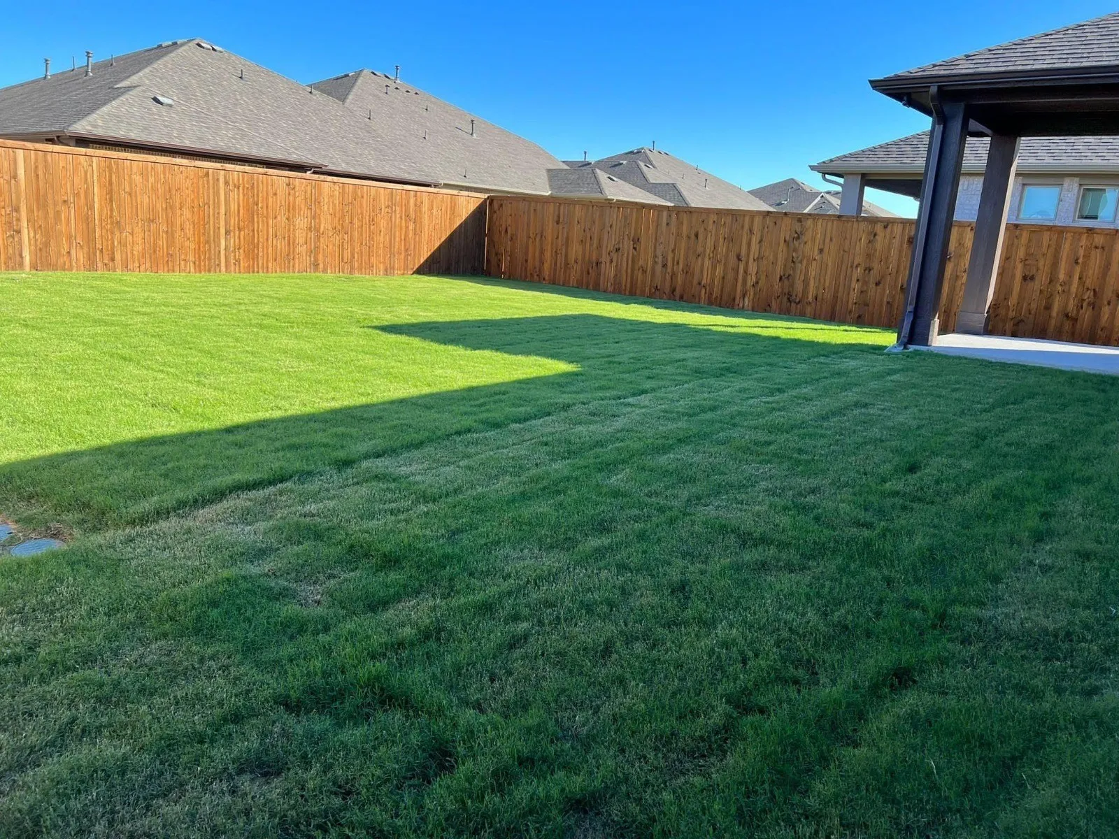 Expansive backyard featuring a lush lawn, privacy fencing, and a covered patio with concrete flooring