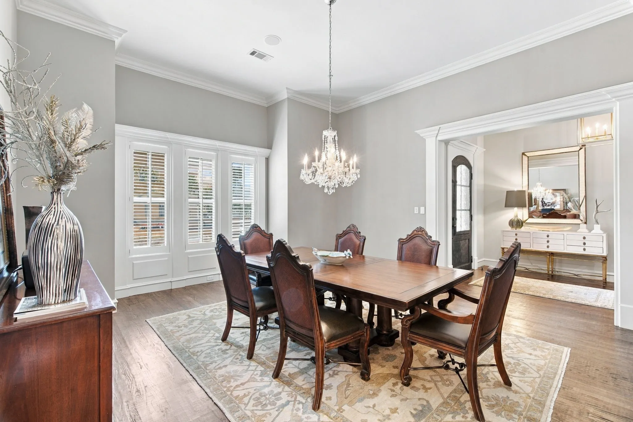 Wood-finish flooring, crown molding, and a crystal chandelier illuminate this formal dining area