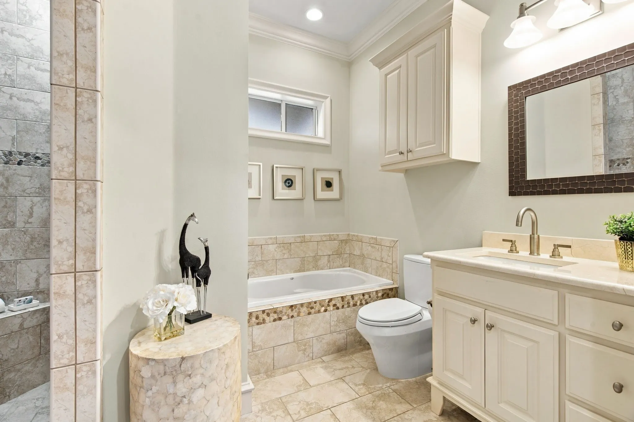 Tile-surrounded soaking tub, vanity with built-in cabinetry, tiled shower with accent band, and recessed lighting