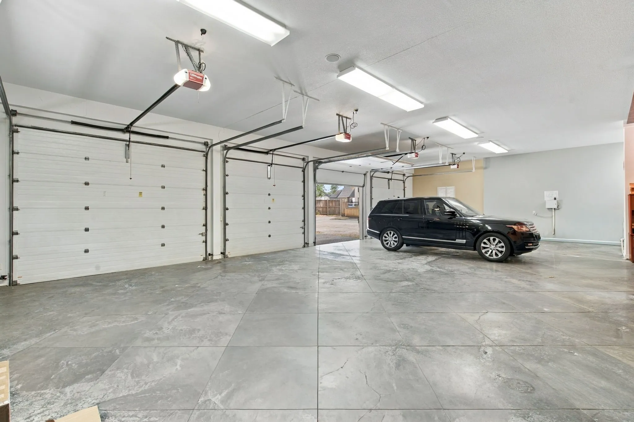Spacious garage featuring four overhead doors, concrete flooring, and ample overhead lighting