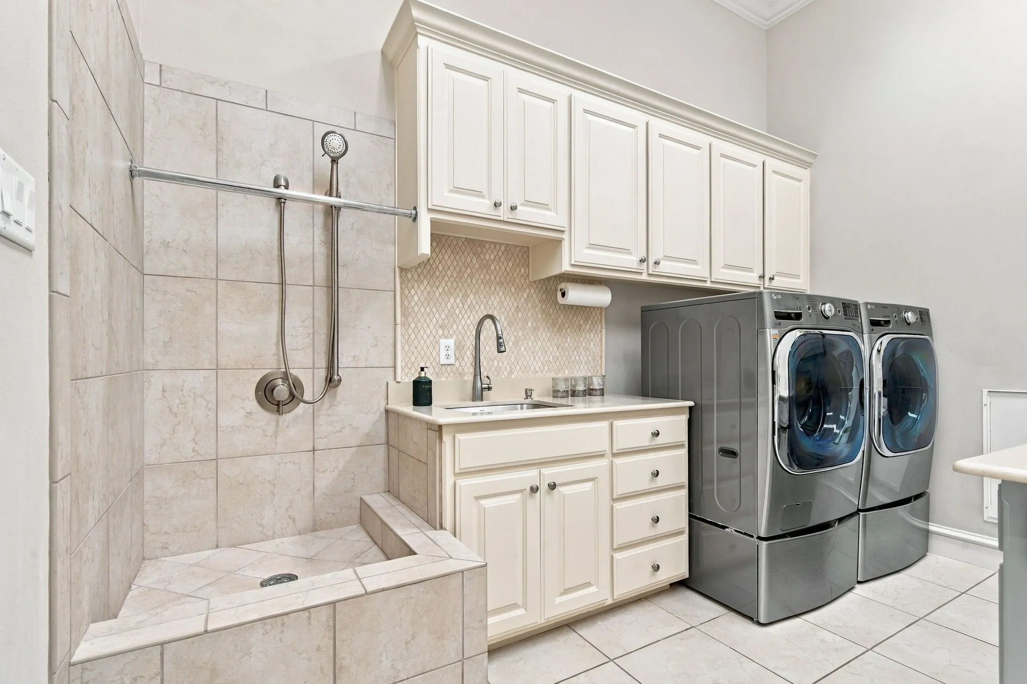 Built-in utility shower with tiled surround, shaker-style cabinetry with crown molding, countertop utility sink, and tiled​​‌​​​​‌​​‌‌​‌‌​​​‌‌​‌​‌​‌​​​‌​​ flooring