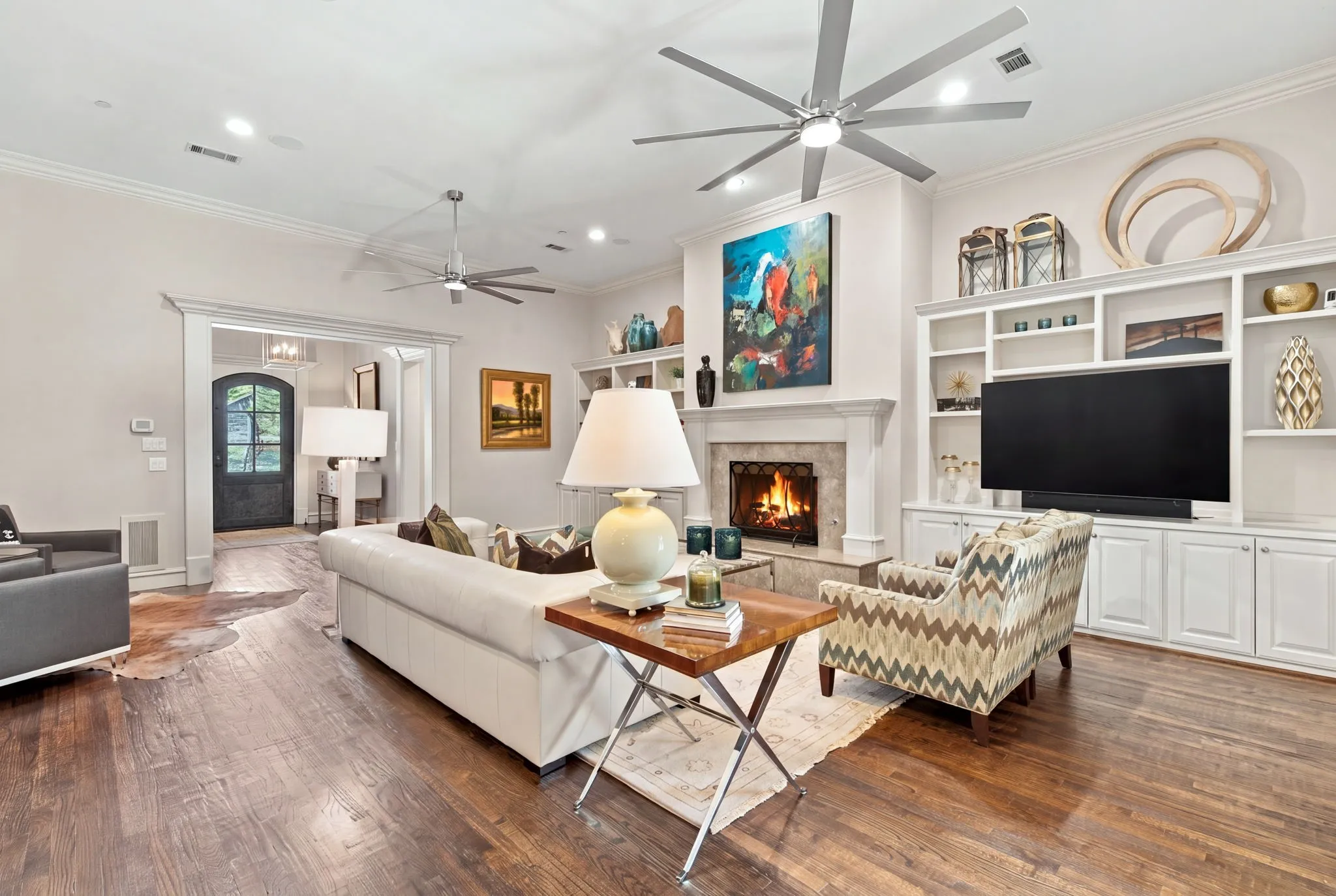 Hardwood flooring, crown molding, built-in shelving, stone fireplace, and ceiling fans