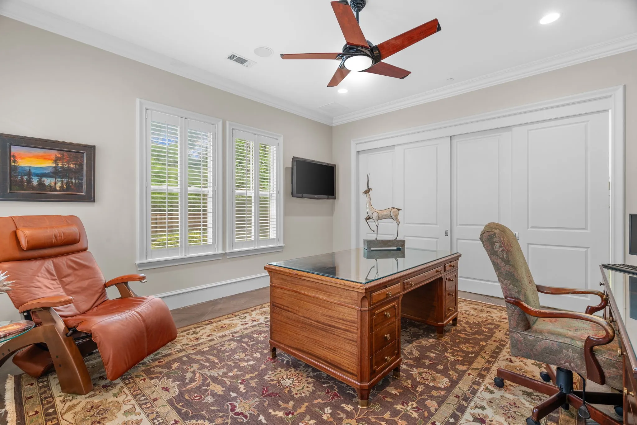 Recessed lighting, crown molding, and a ceiling fan fixture illuminate this space, which features a pair of windows with plantation shutters and a sliding closet