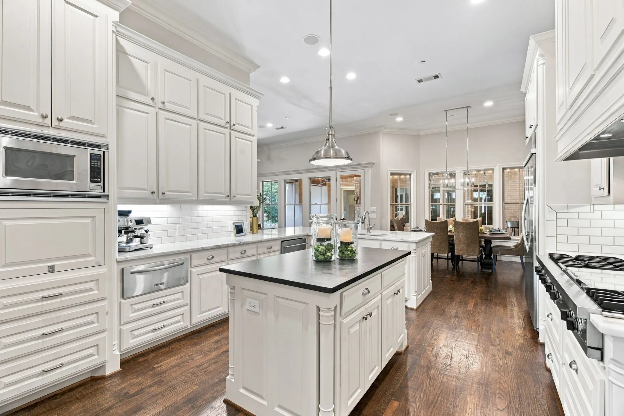 White cabinetry with crown molding, stainless steel appliances, dark wood-finish flooring, white subway tile backsplash, and a central island with a dark countertop