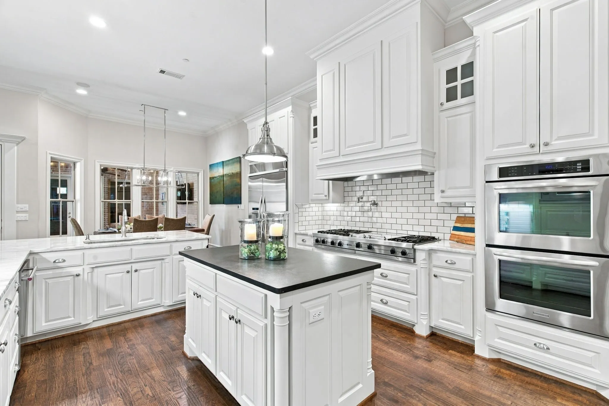 Gourmet kitchen with white cabinetry, stainless steel double ovens, gas range, brick pattern backsplash, and a central island with a contrasting countertop