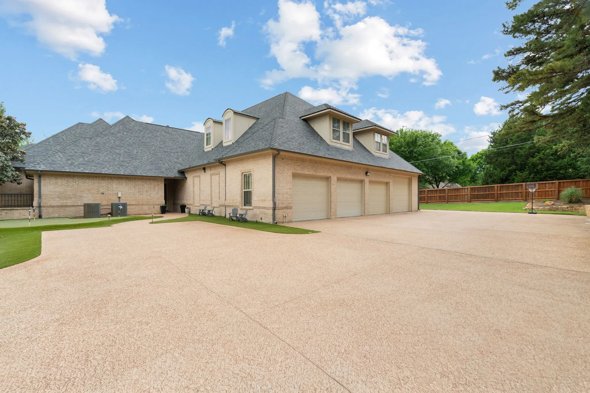 Exterior featuring a brick facade, four garage doors, a dormer roof, a shingle roof, and an expansive paved driveway