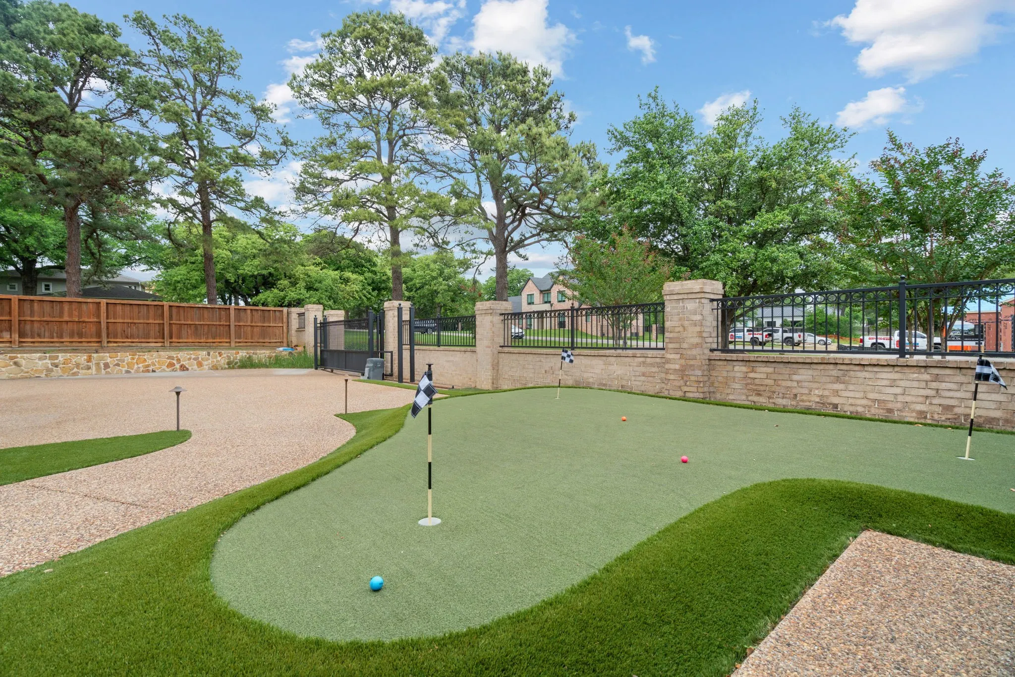 Private putting green with artificial turf, stone border walls, and a gravel driveway