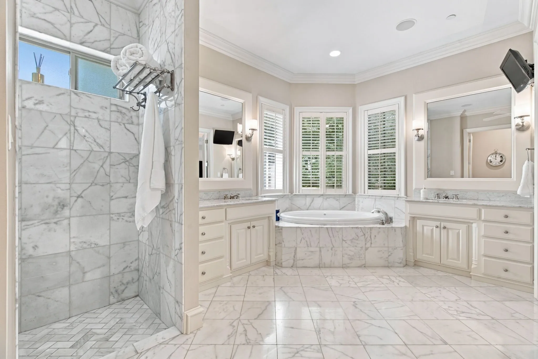 Spacious bathroom featuring marble tile flooring, a large soaking tub with marble surround, an expansive walk-in shower with marble tile, and dual vanities with integrated sinks