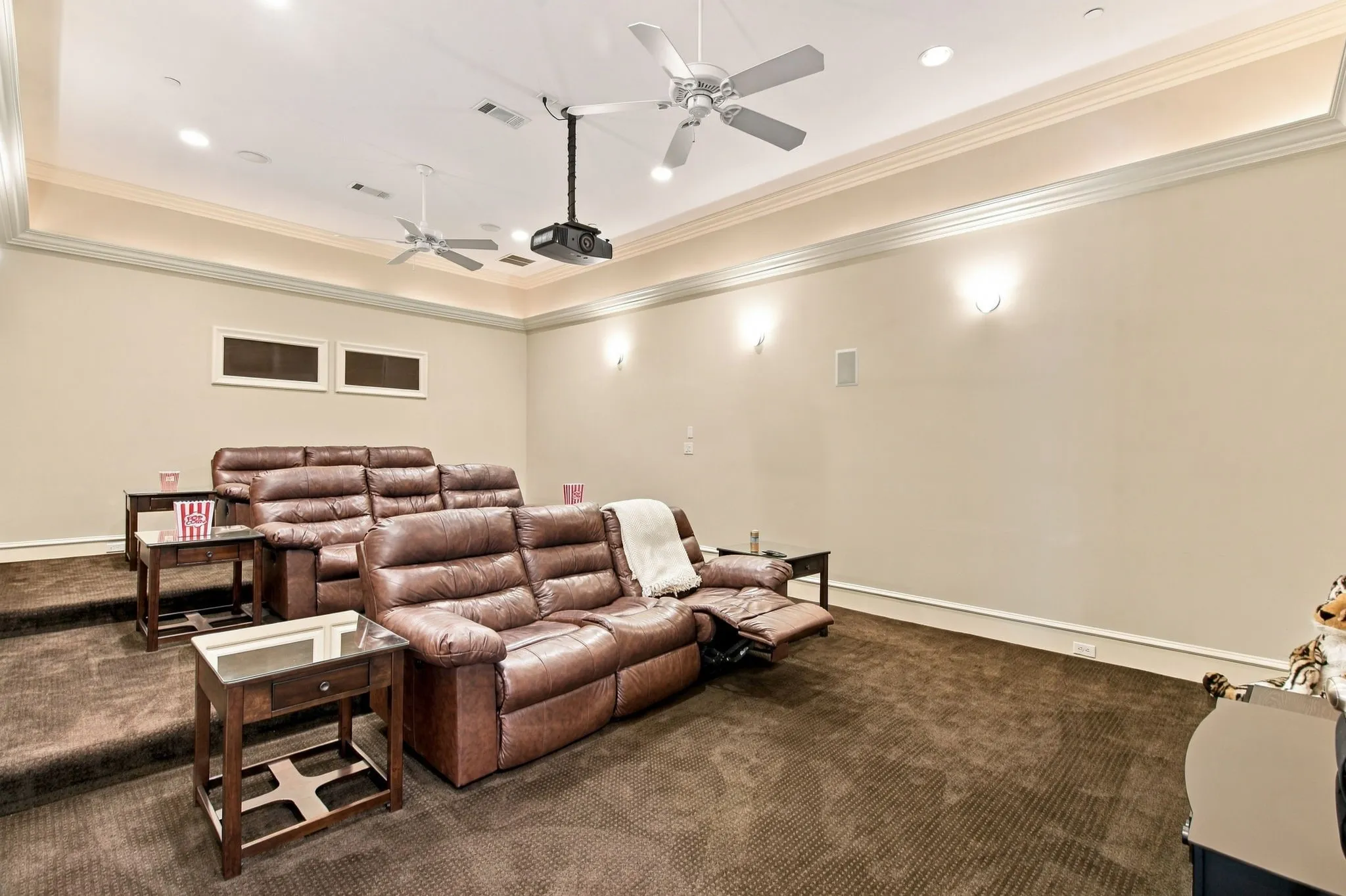 Dedicated media room featuring tiered flooring, recessed lighting, ceiling fans, and a ceiling-mounted projector