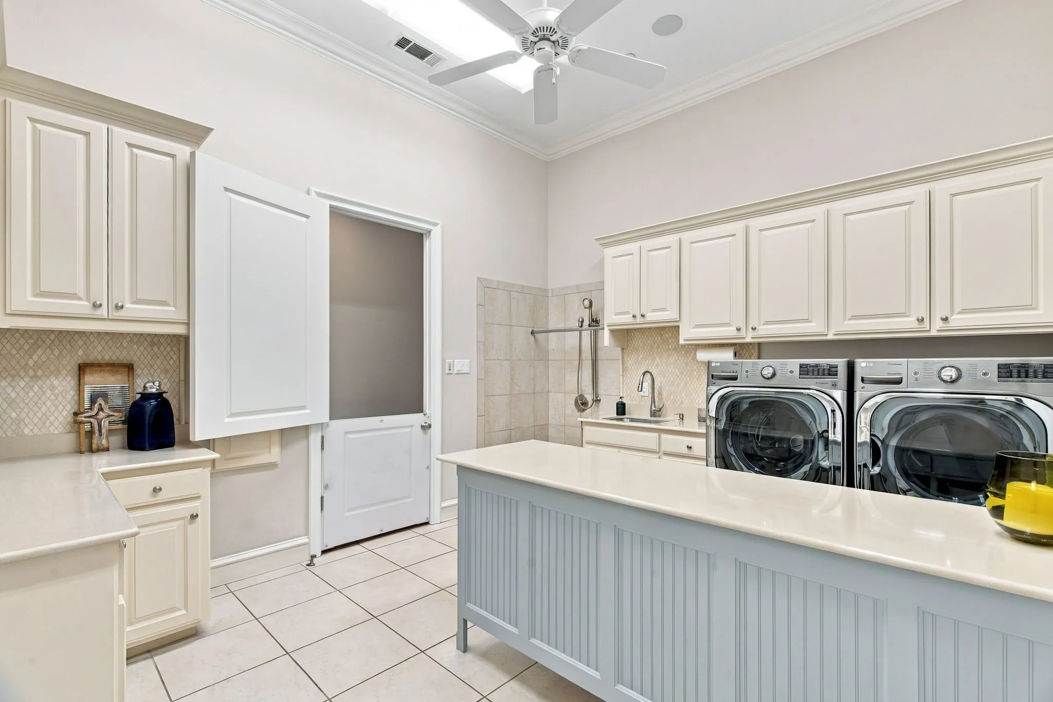 Laundry room featuring light-colored cabinetry, a Dutch door, tiled flooring, a built-in sink, and a central island with a light-colored countertop
