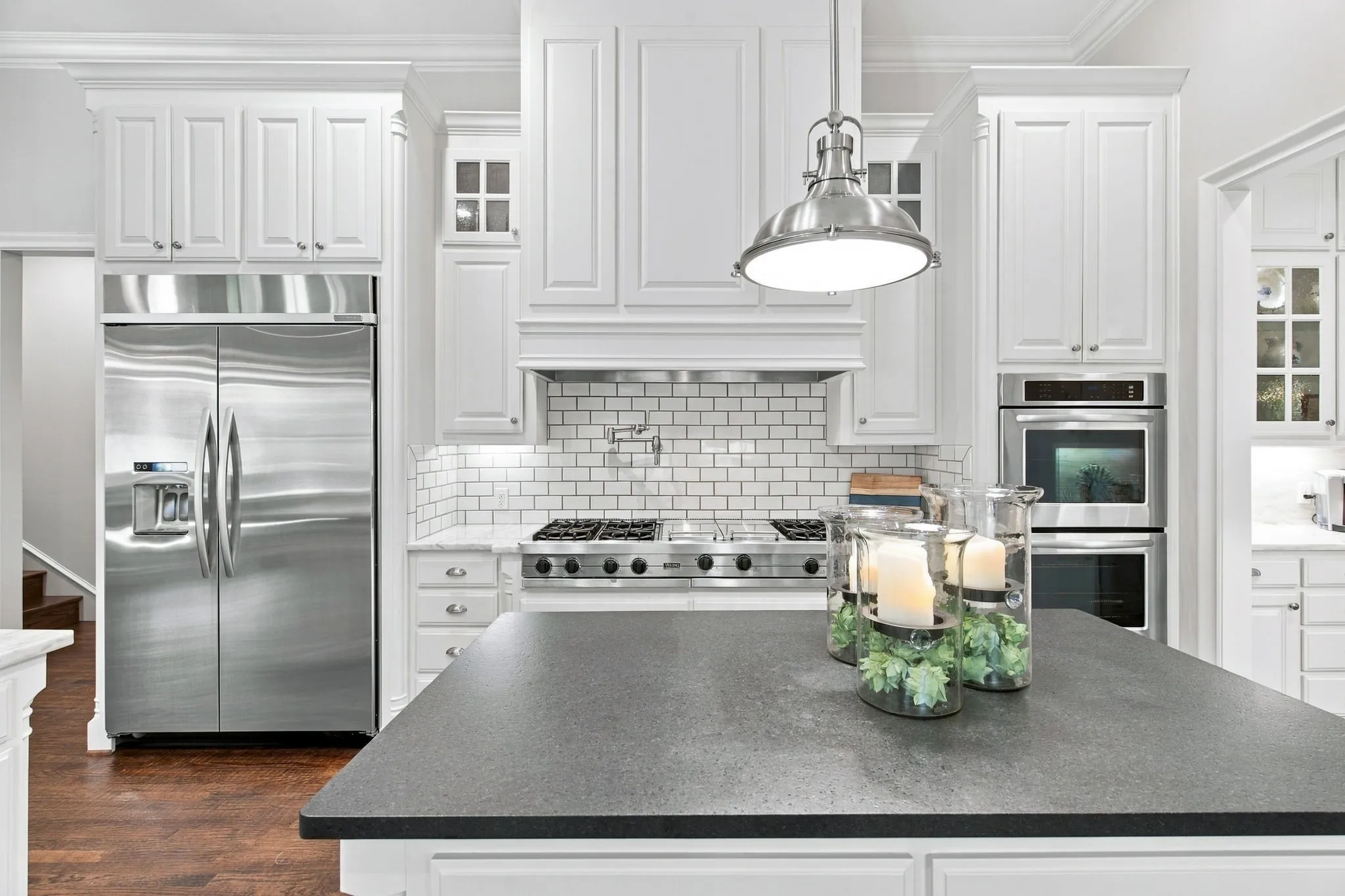 White cabinetry, stainless steel appliances, subway tile backsplash, dark countertop island, and wood-finish flooring
