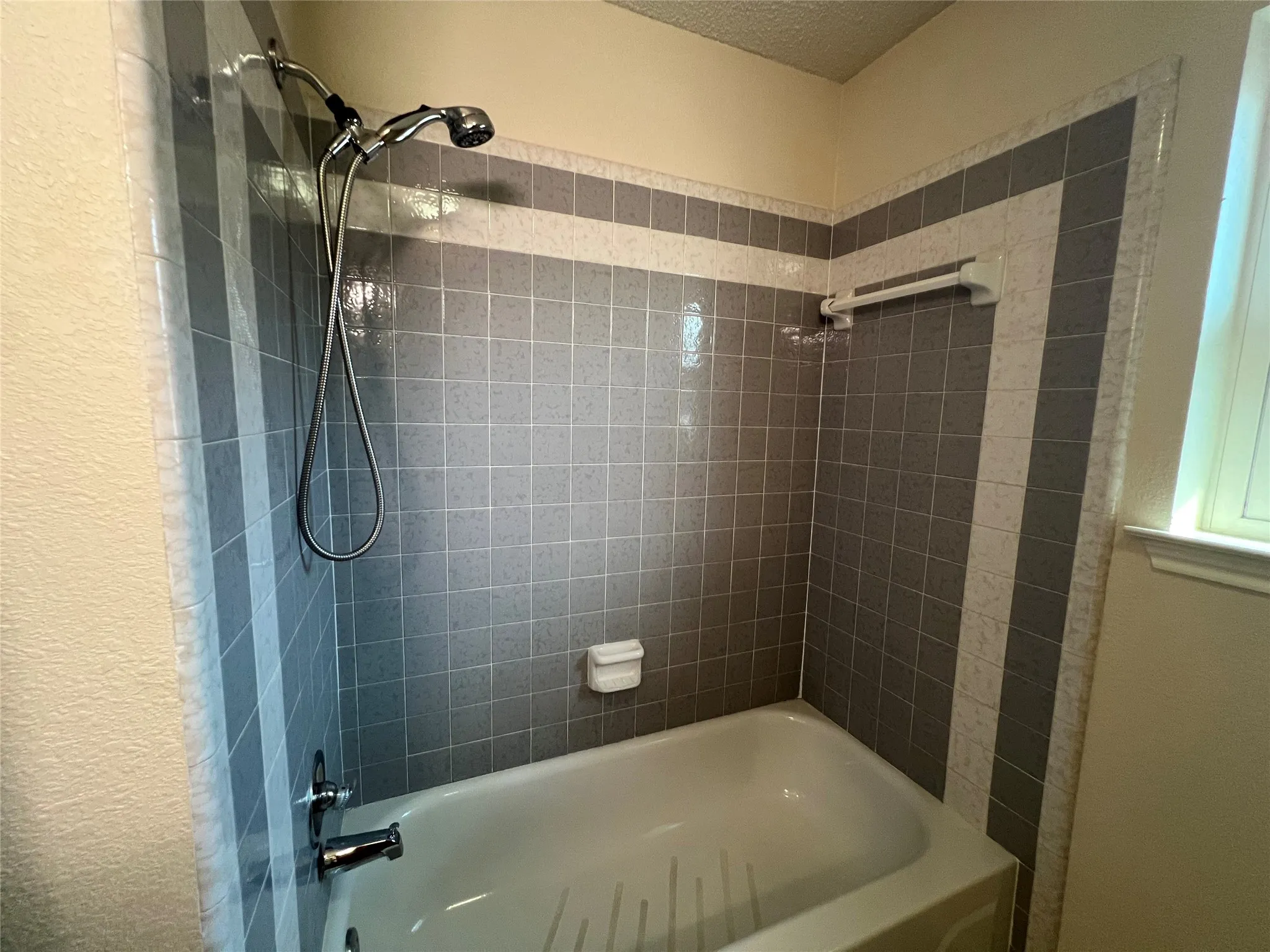 Bathtub with a tiled surround featuring a geometric pattern, chrome fixtures, and a handheld showerhead