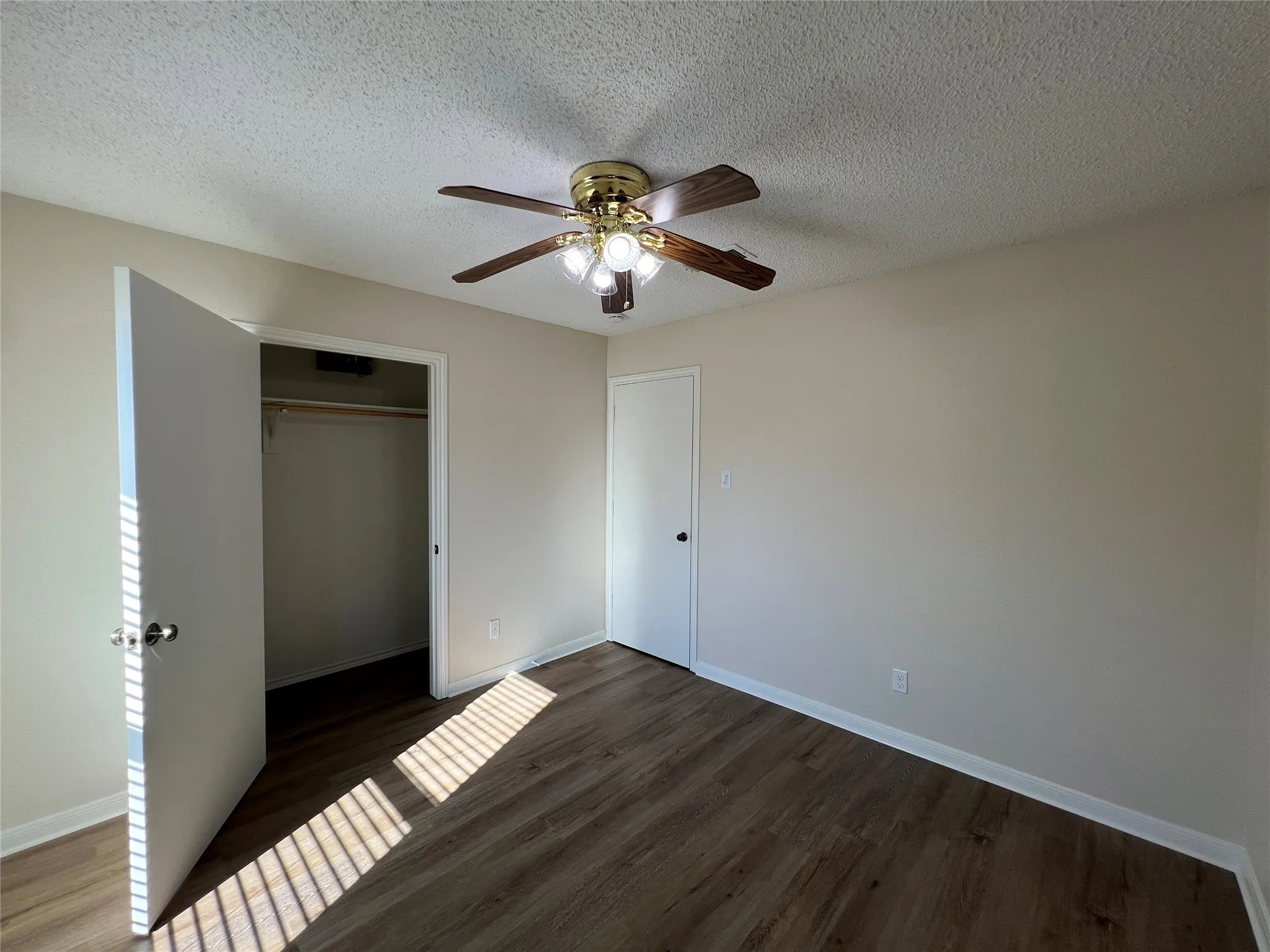 Wood-finish flooring, ceiling fan with integrated lighting, built-in closet with hanging rod, neutral wall color, and white trim