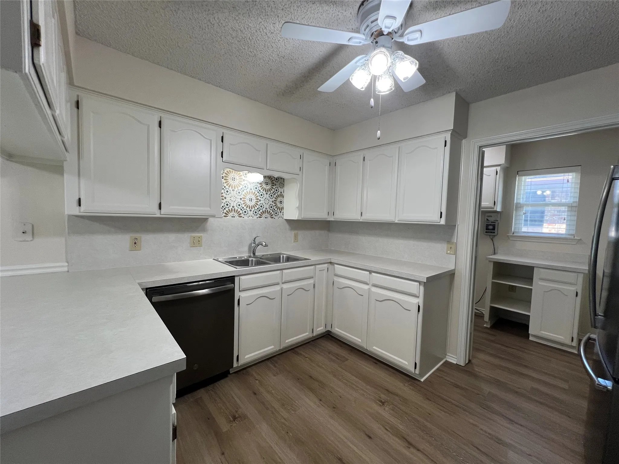 Kitchen featuring white cabinetry, gray countertops, stainless steel sink, patterned backsplash, and wood-finish flooring
