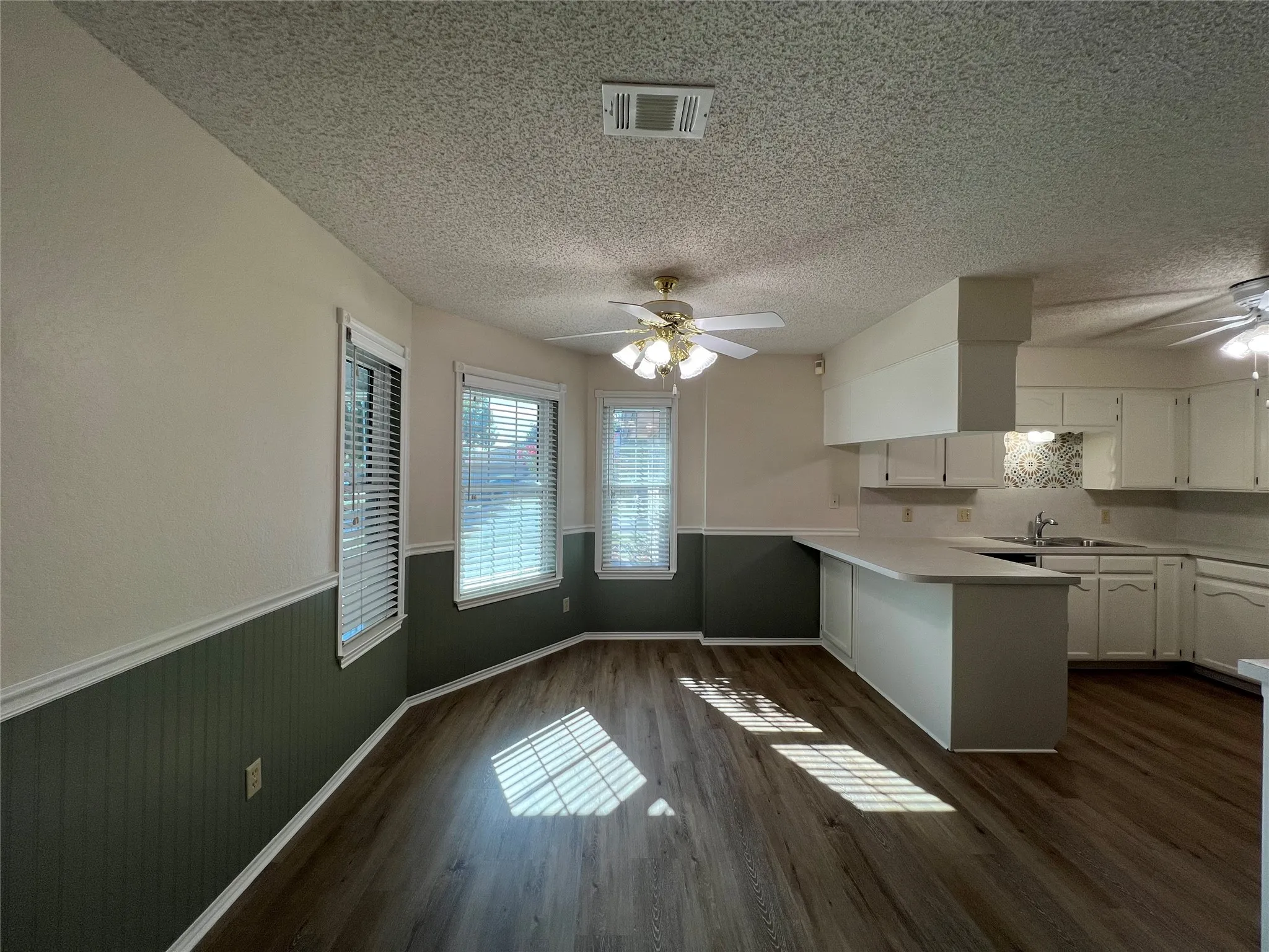 Wood-finish flooring throughout, white upper and lower cabinetry, white kitchen countertops, patterned tile backsplash, and two ceiling fans with integrated lighting