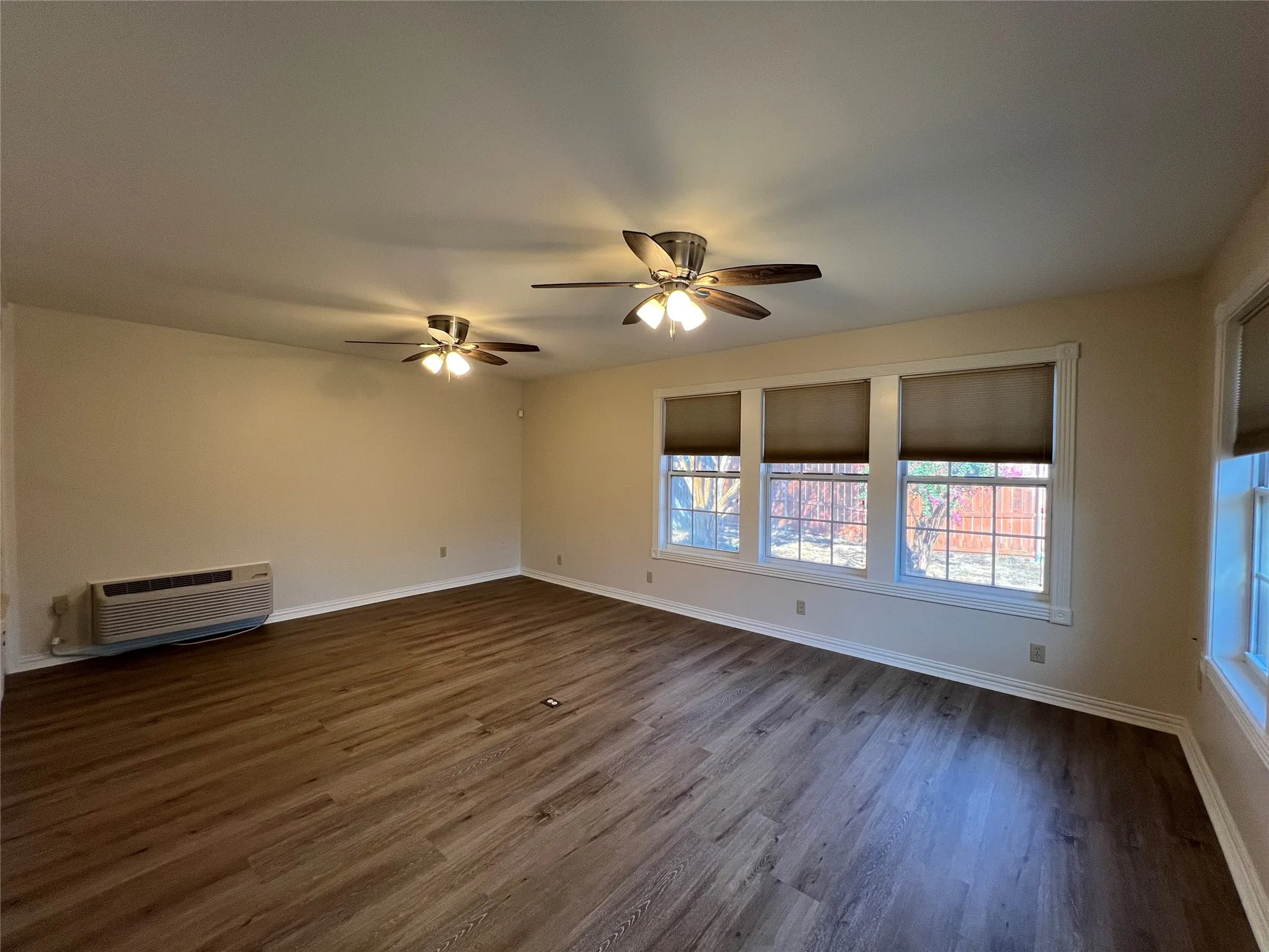 Spacious room featuring wood-finish flooring, multiple windows, and two ceiling fans with integrated lighting