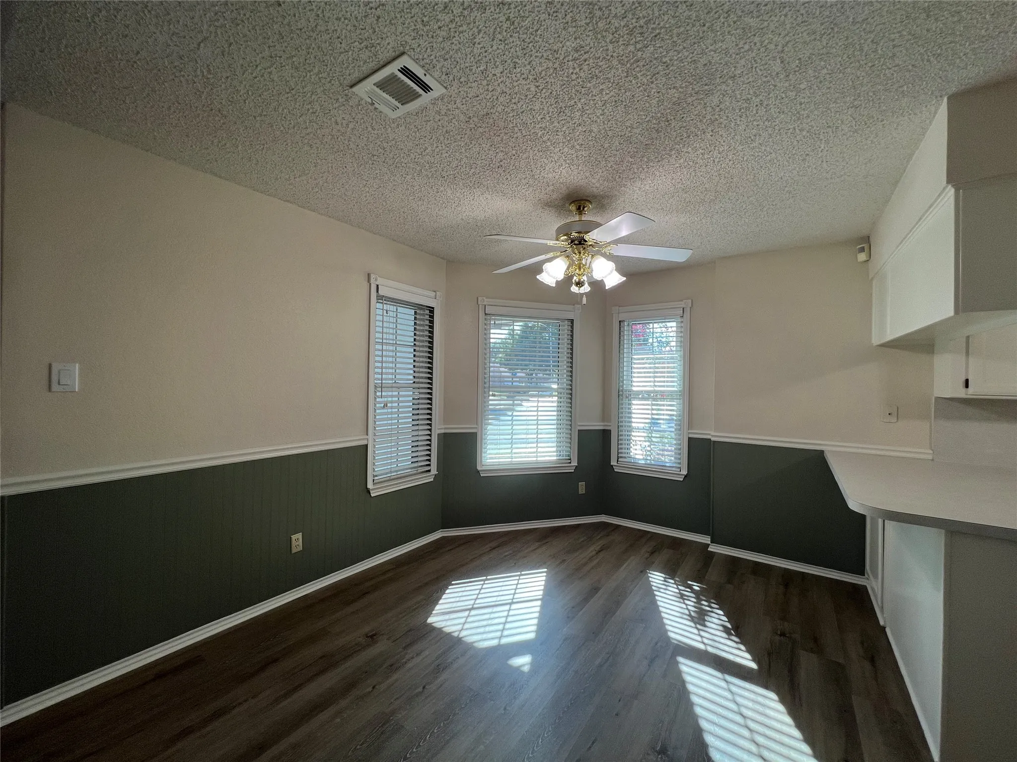 Wood-finish flooring, accent wainscoting, multiple windows with blinds, ceiling fan, and built-in cabinetry