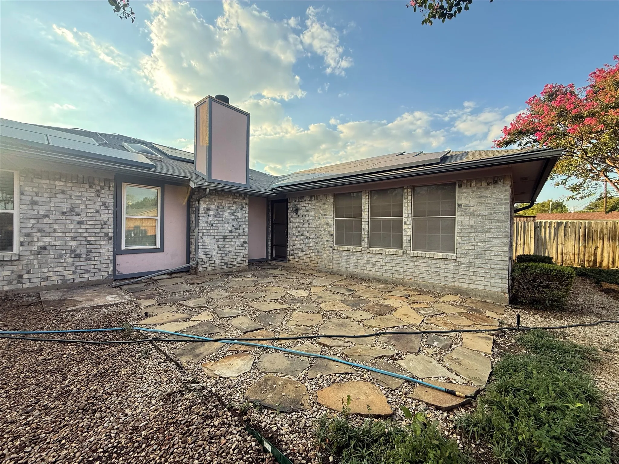 Flagstone patio with a light gray brick exterior, multiple windows, and a prominent chimney