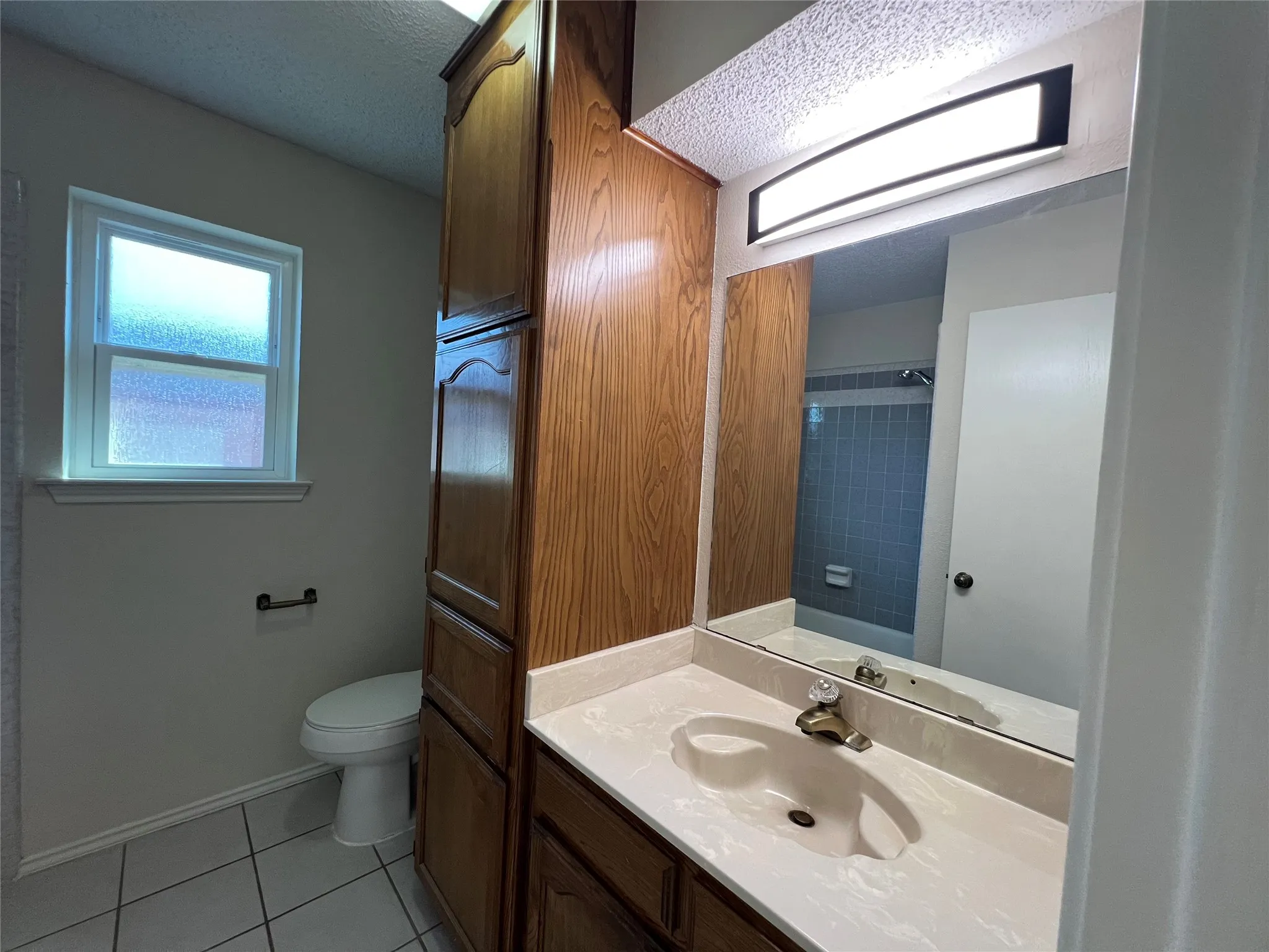 Built-in cabinetry, vanity with integrated sink, rectangular mirror, overhead vanity lighting, and ceramic tile flooring