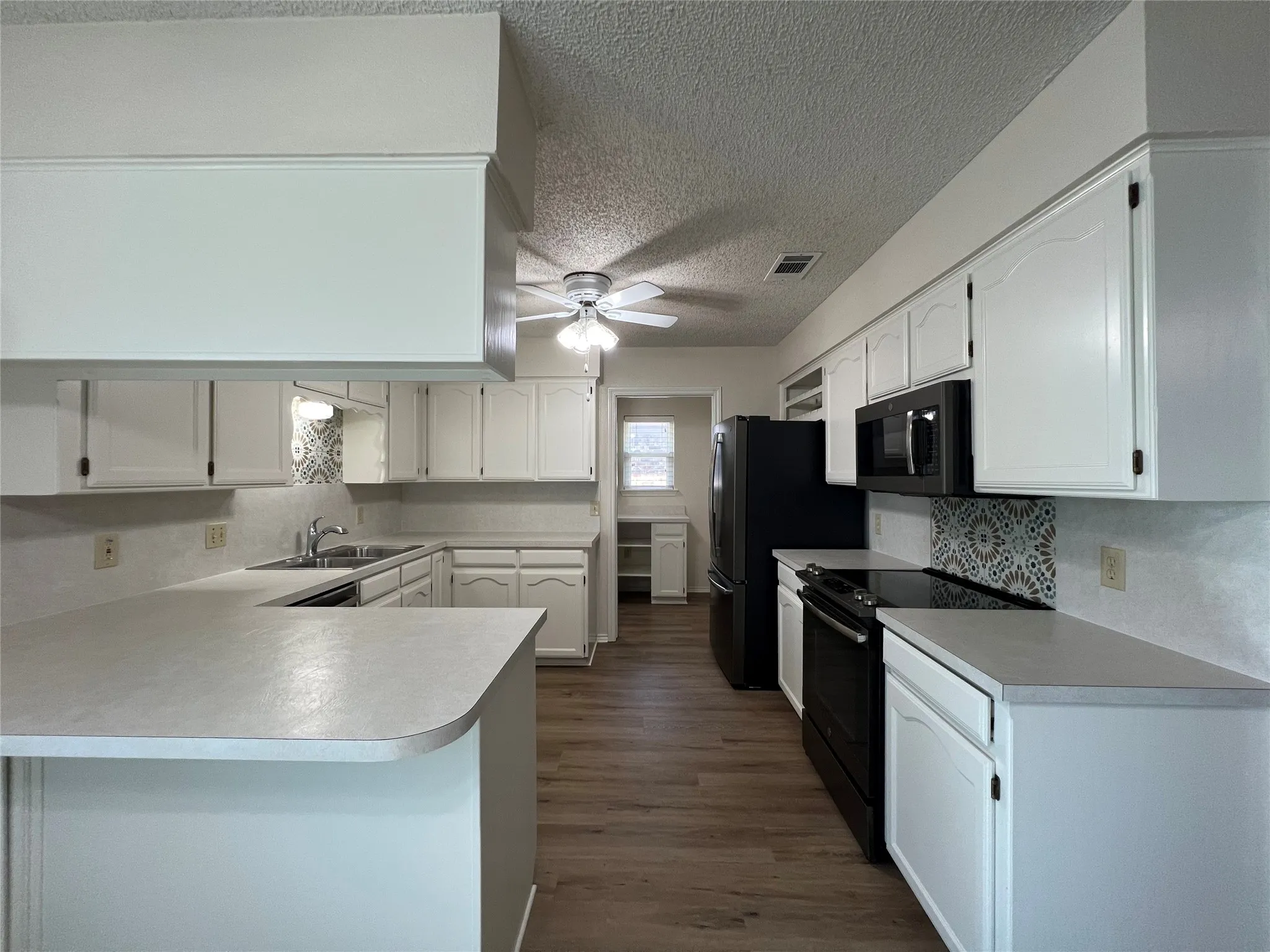 Kitchen featuring white cabinetry, wood-finish flooring, a ceiling fan, and black appliances