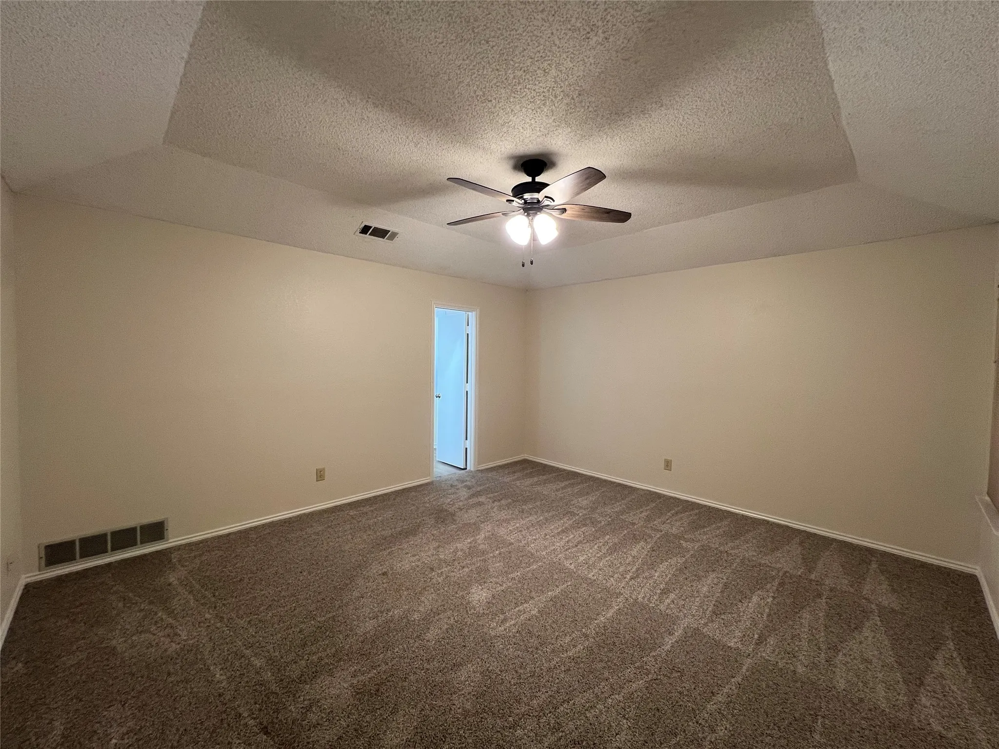 Spacious room featuring a tray ceiling, ceiling fan with integrated lighting, and patterned carpet flooring