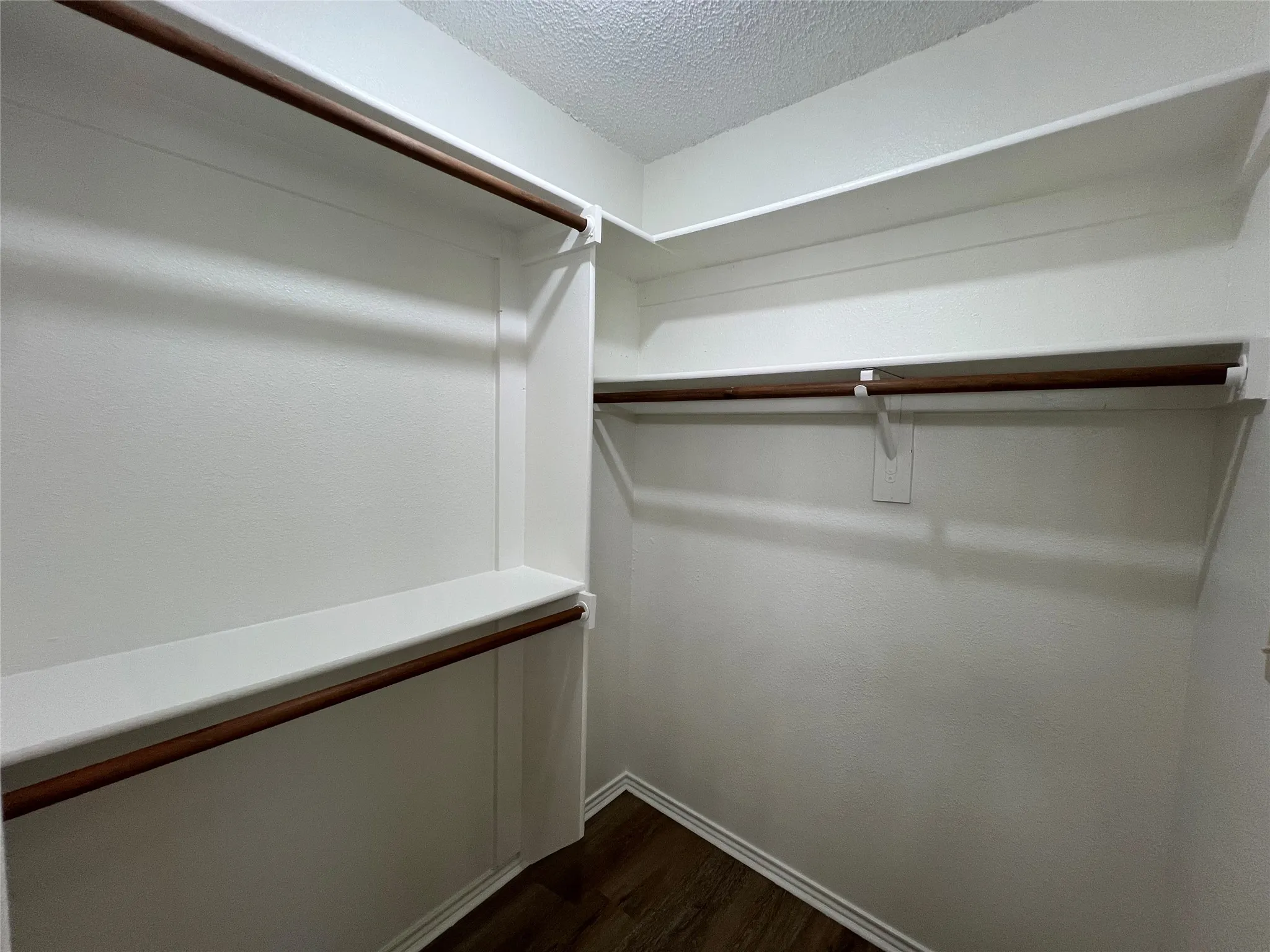 Built-in white shelving and wooden clothing rods on multiple walls, complemented by wood-finish flooring