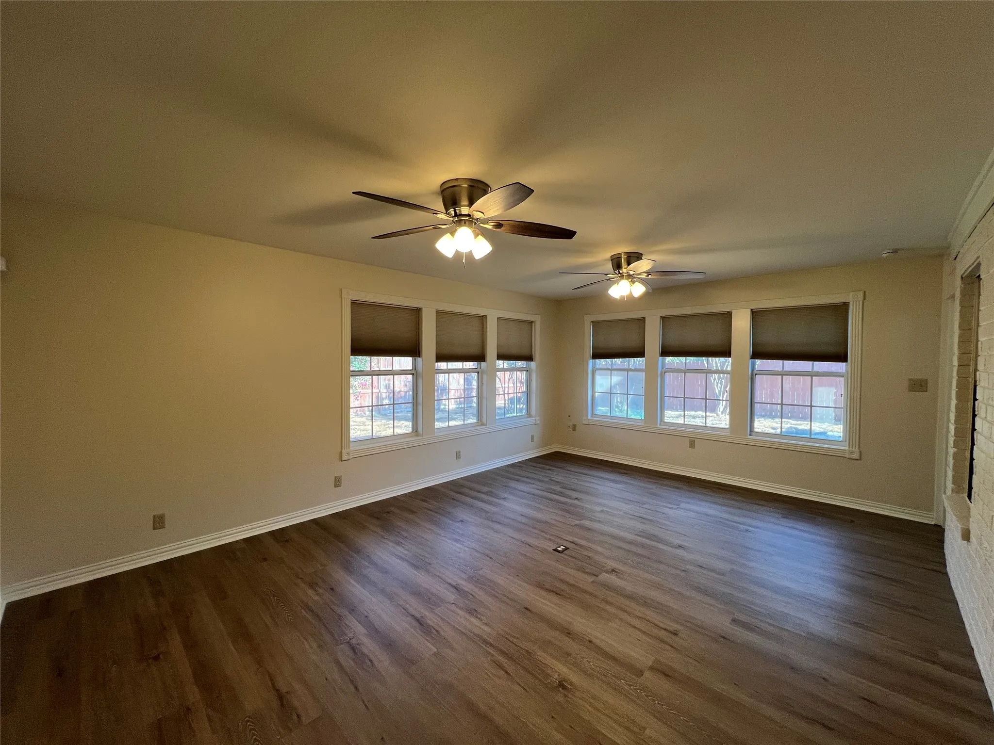Wood-finish flooring, multiple windows with blinds, two ceiling fans with integrated lighting, and painted walls