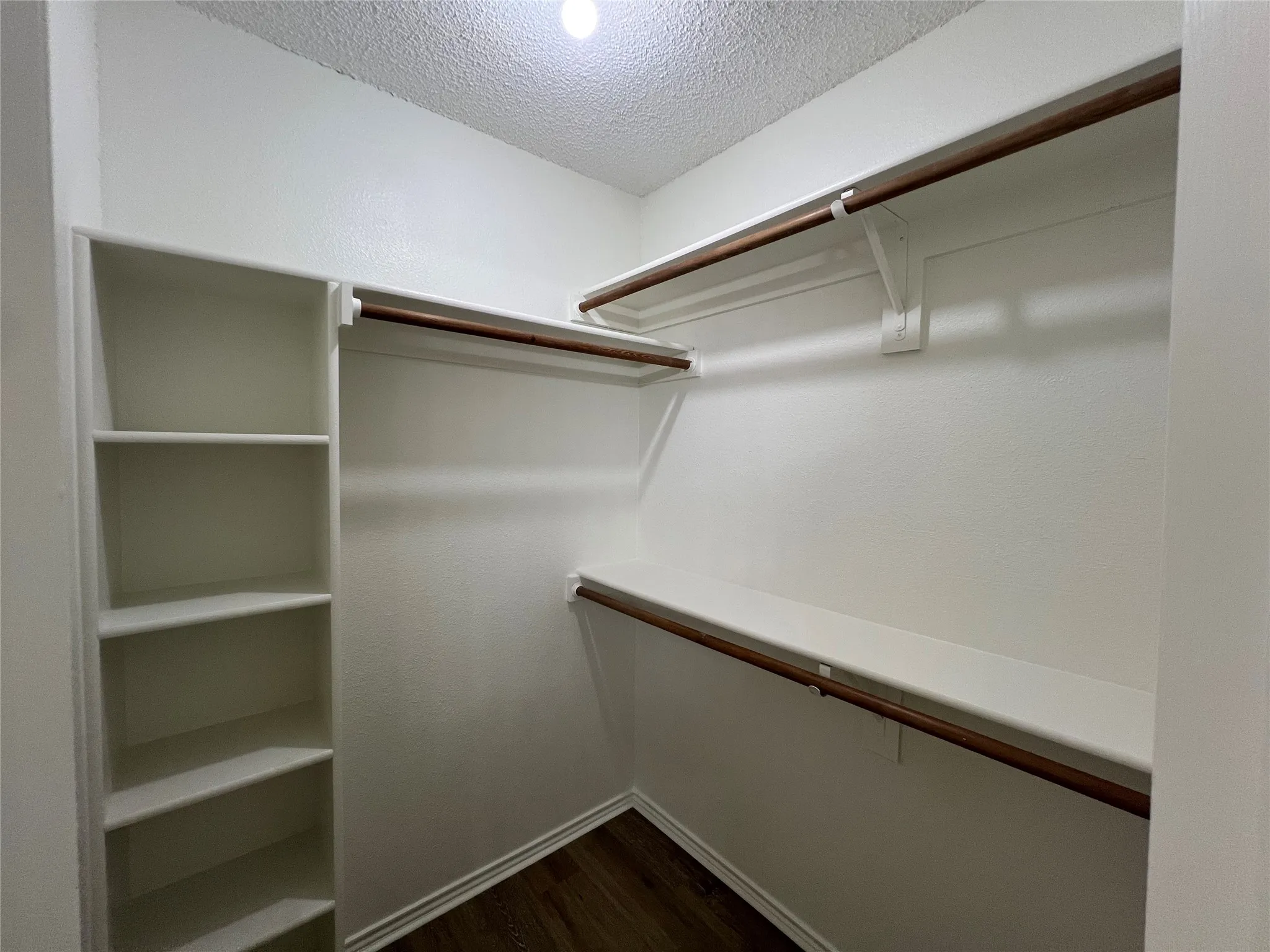 Walk-in closet featuring wood-finish flooring, built-in shelving, and multiple hanging rods
