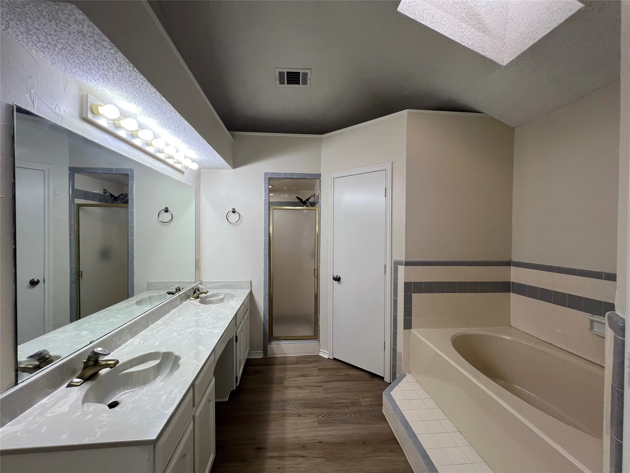 Wood-finish flooring with a dual vanity, large wall mirror, and a built-in tub