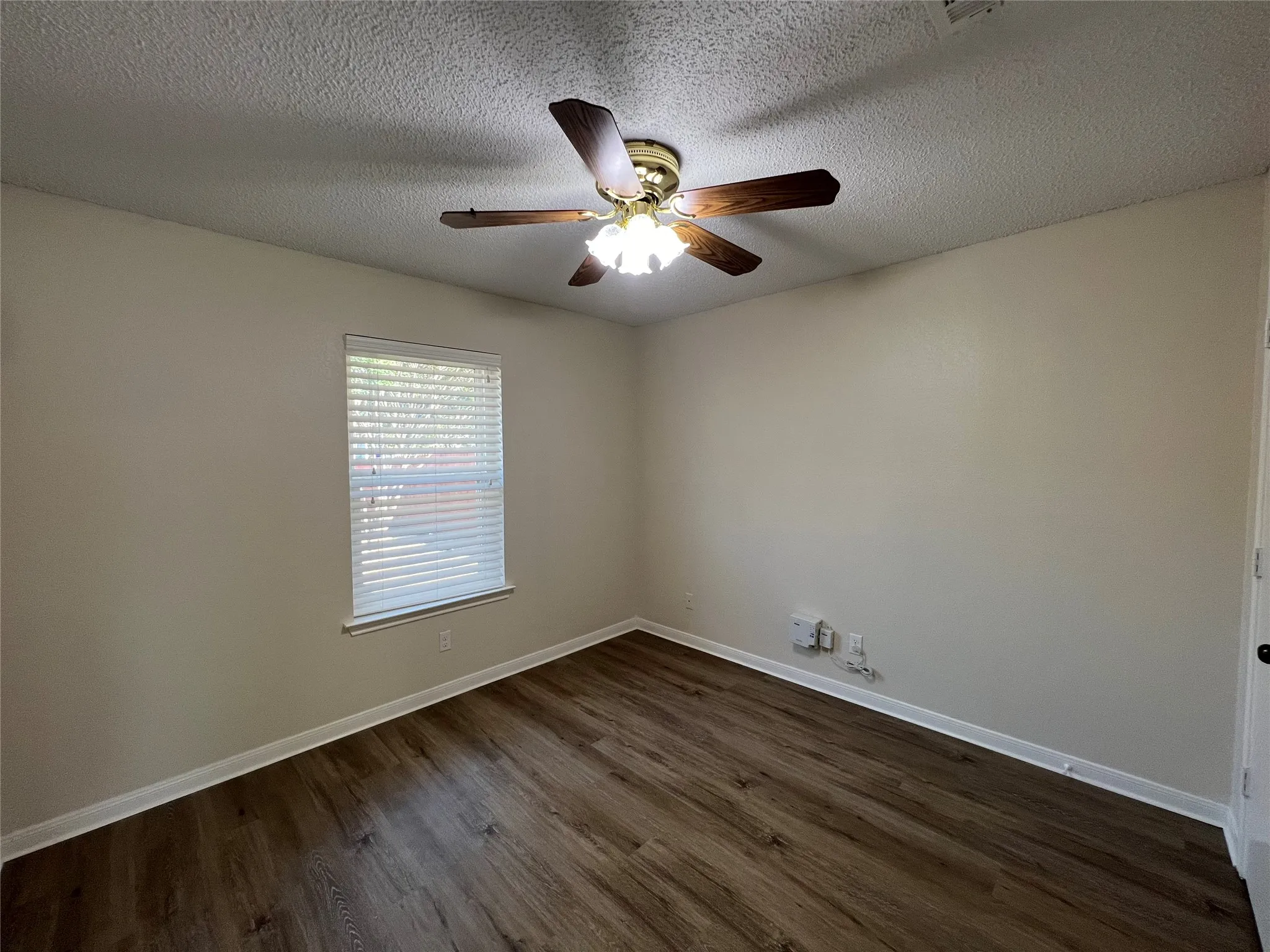 Wood-finish flooring, neutral wall tones, window with horizontal blinds, and a ceiling fan with integrated lighting