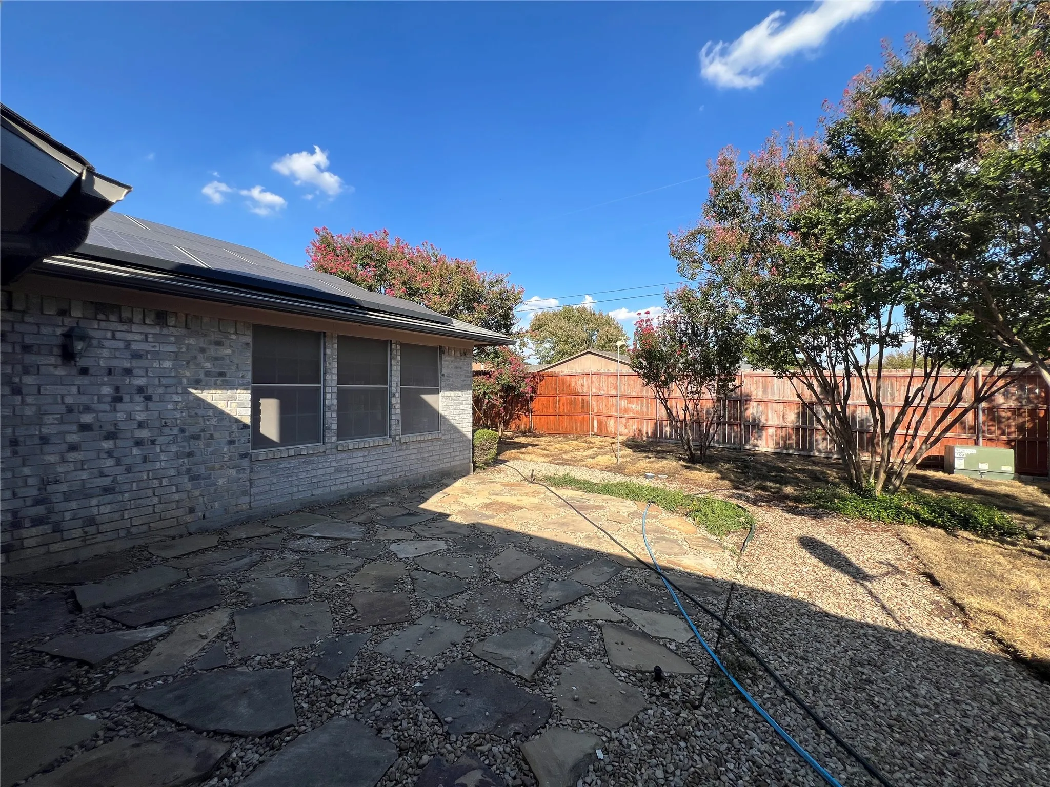 Stone patio area, brick exterior, solar panels, mature trees, and privacy fencing