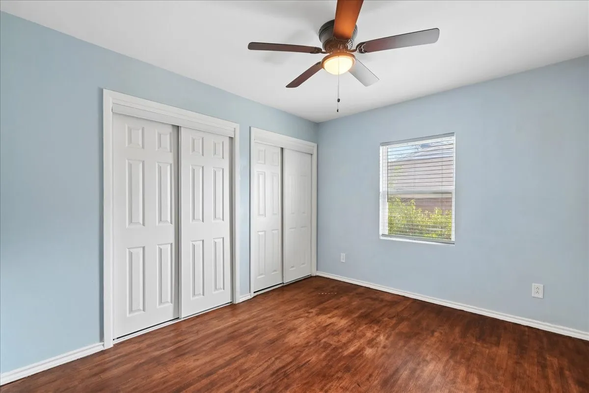Wood-finish flooring, two sliding panel closets, ceiling fan with integrated lighting, and a window with blinds