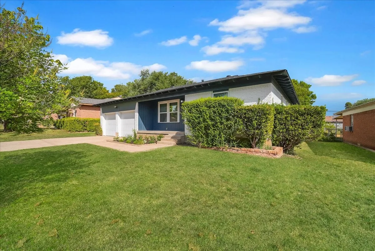 Brick and siding exterior with a dark roof, concrete driveway, and established front landscaping