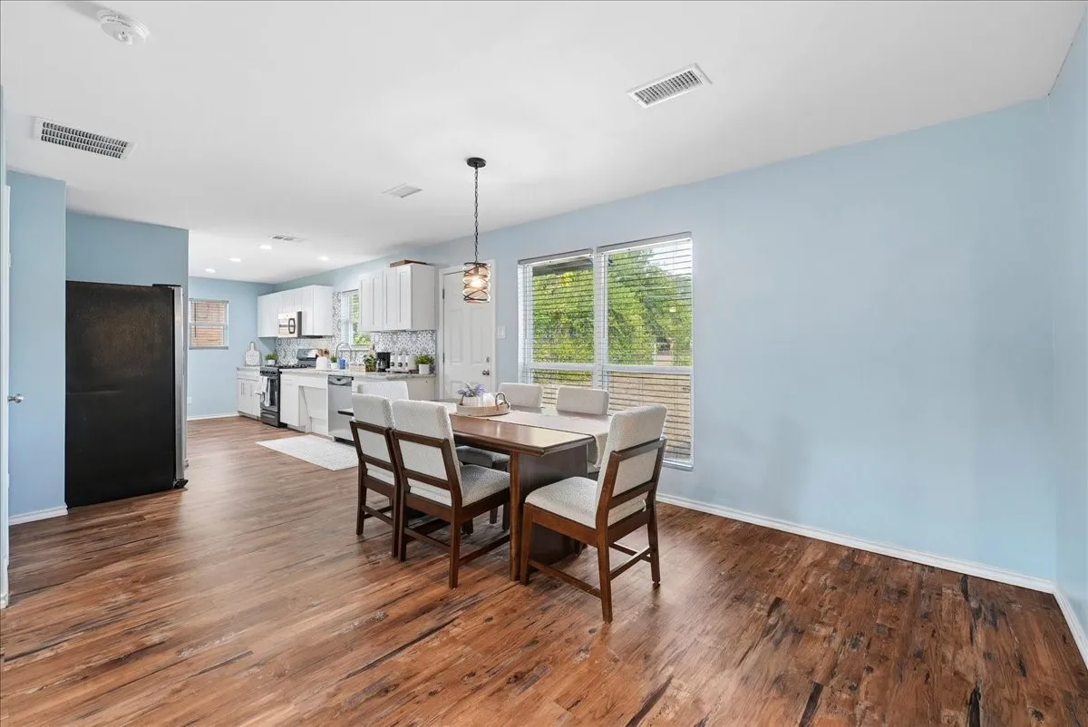 Wood-finish flooring throughout, white upper and lower cabinetry, white appliances, and a pendant light fixture