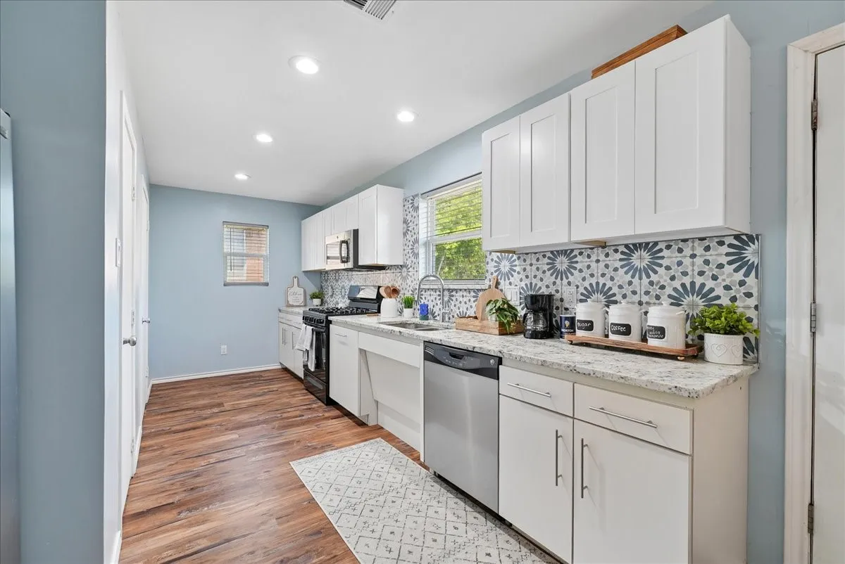 Kitchen featuring wood-finish flooring, white cabinetry, integrated stainless steel appliances, a patterned tile backsplash, and recessed lighting