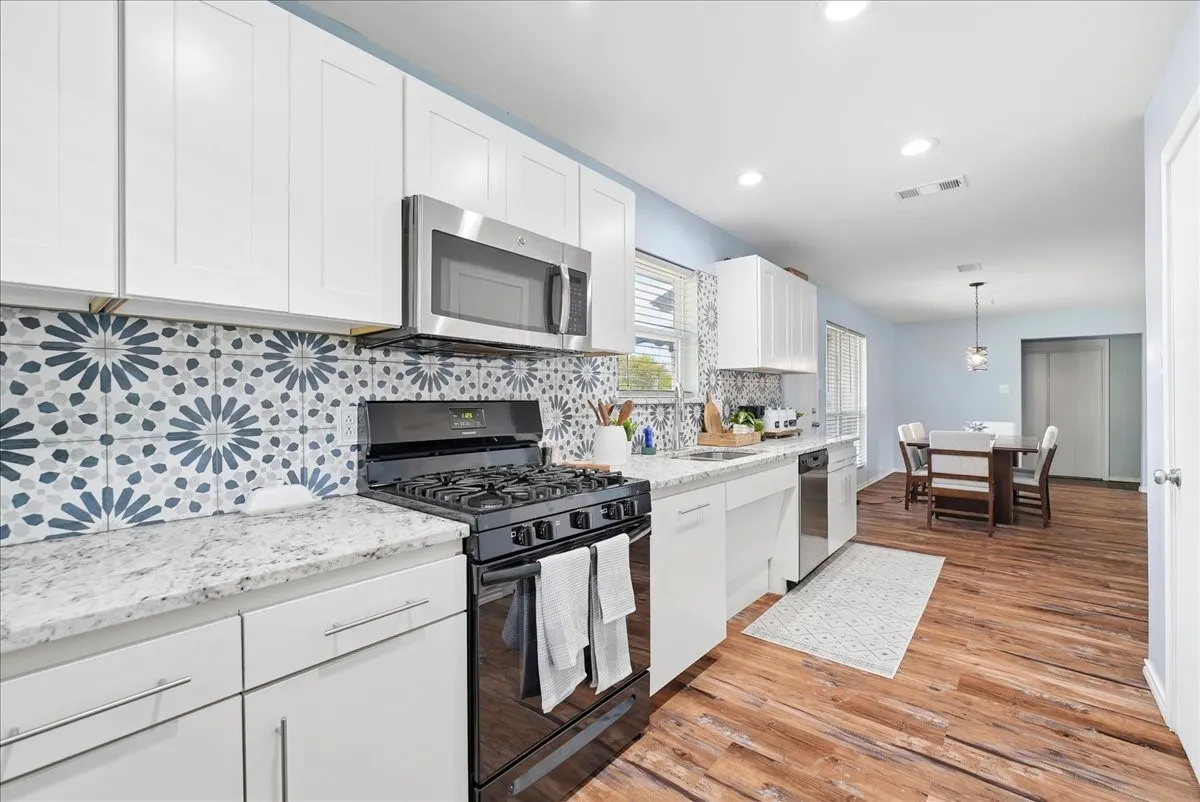 White shaker cabinetry, patterned tile backsplash, stainless steel appliances, granite countertops, and wood-finish flooring