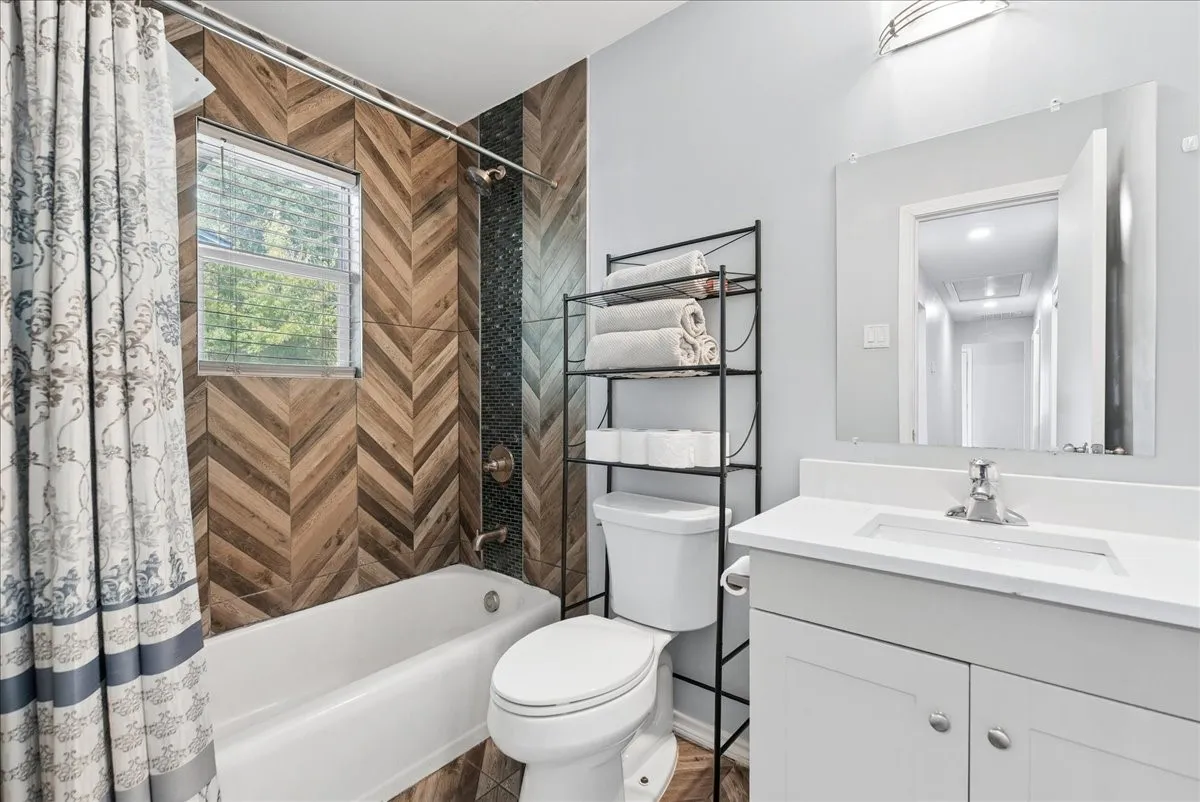 Bathroom featuring a wood-finish chevron accent wall, integrated shower/tub, and a vanity with an undermount sink