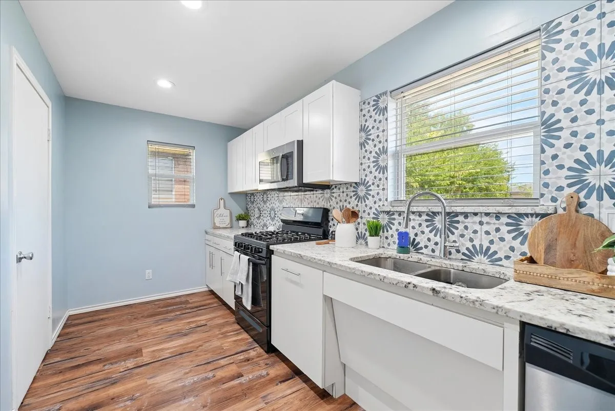 Kitchen featuring wood-finish flooring, white cabinetry, granite countertops, a patterned tile backsplash, and a double-basin stainless steel sink with a gooseneck faucet