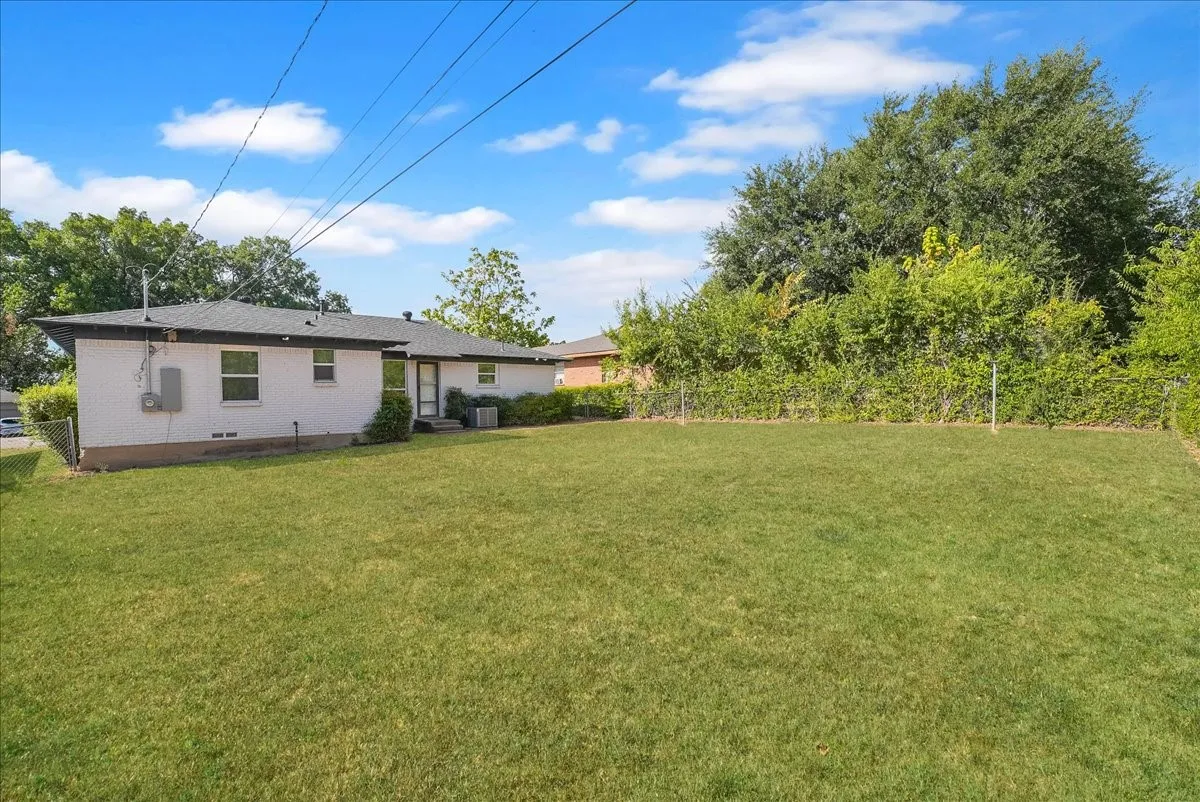 Expansive backyard featuring a manicured lawn, established perimeter foliage, and a chain-link fence