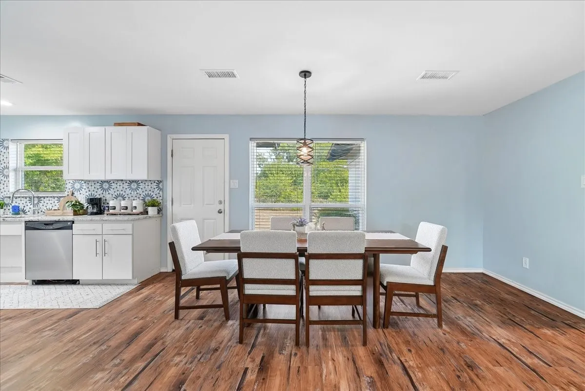 Open-concept living space with wood-finish flooring, a contemporary kitchen featuring white cabinetry, and a dining area illuminated by a decorative pendant light
