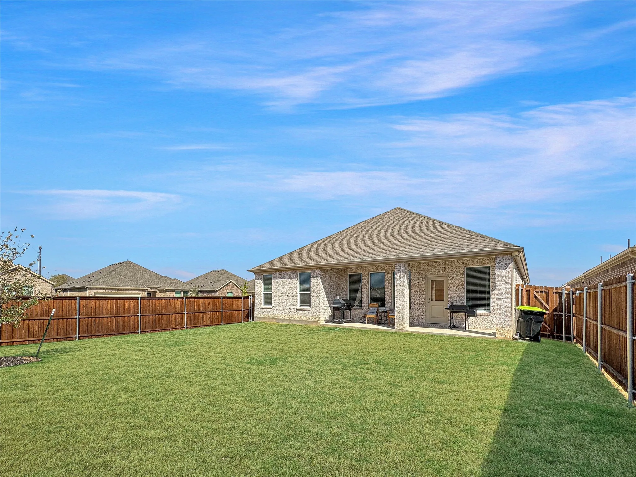 Brick exterior with a covered patio, fenced backyard, and a shingled roof