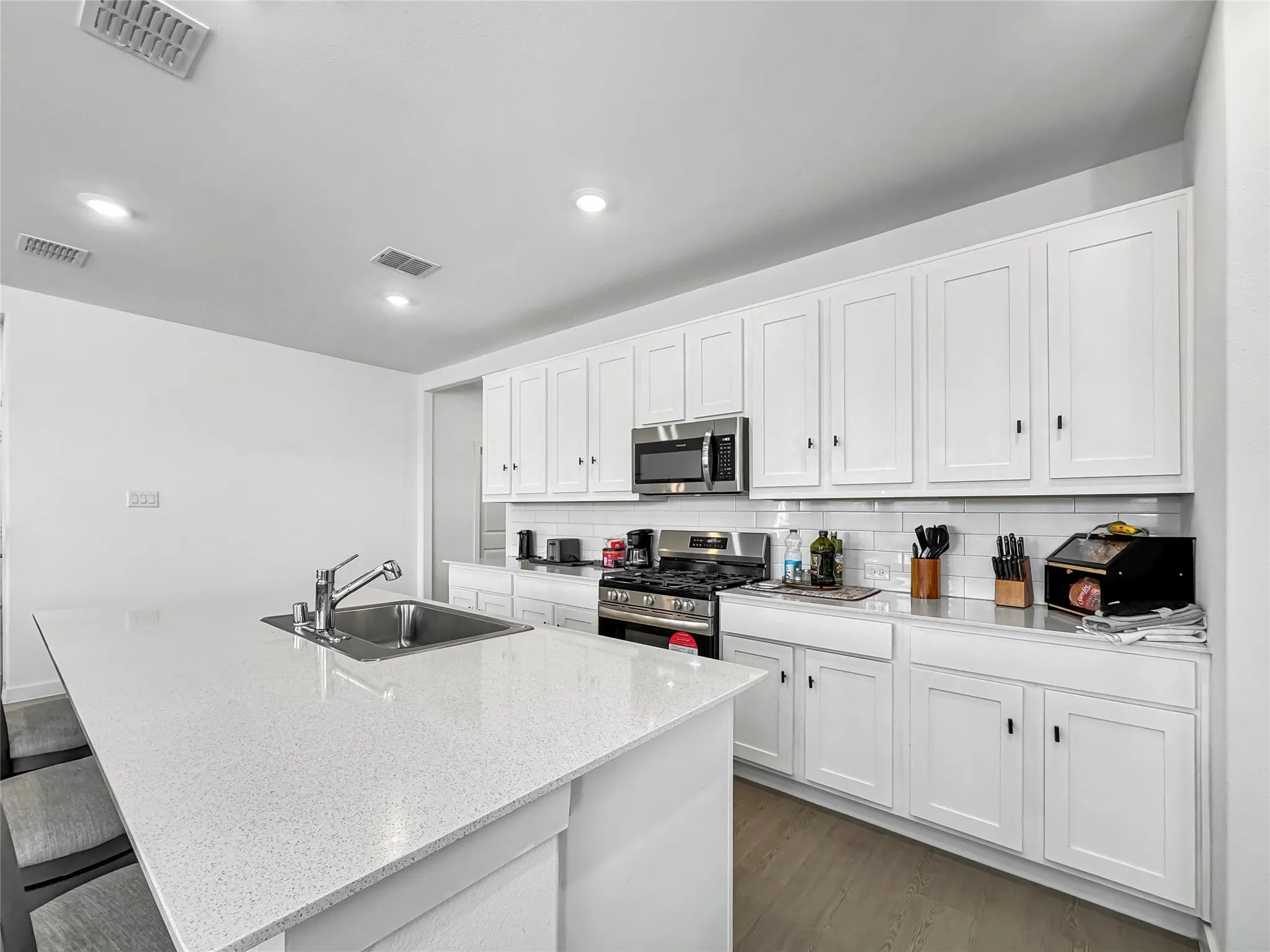 Kitchen featuring a large island with an integrated sink, white shaker-style cabinetry, and stainless steel appliances