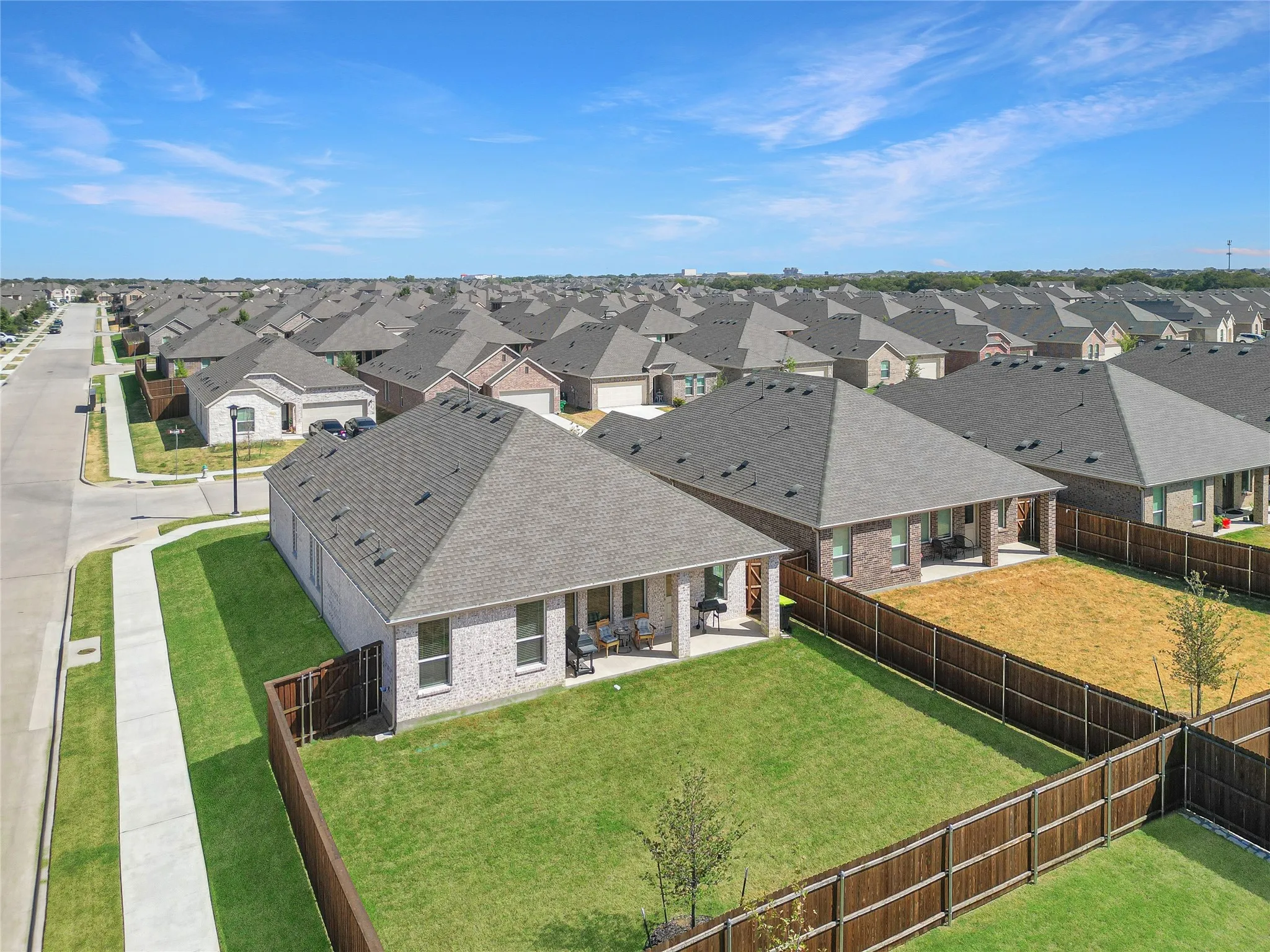 Residential property featuring a shingled roof, brick exterior, and a fenced backyard with a covered patio